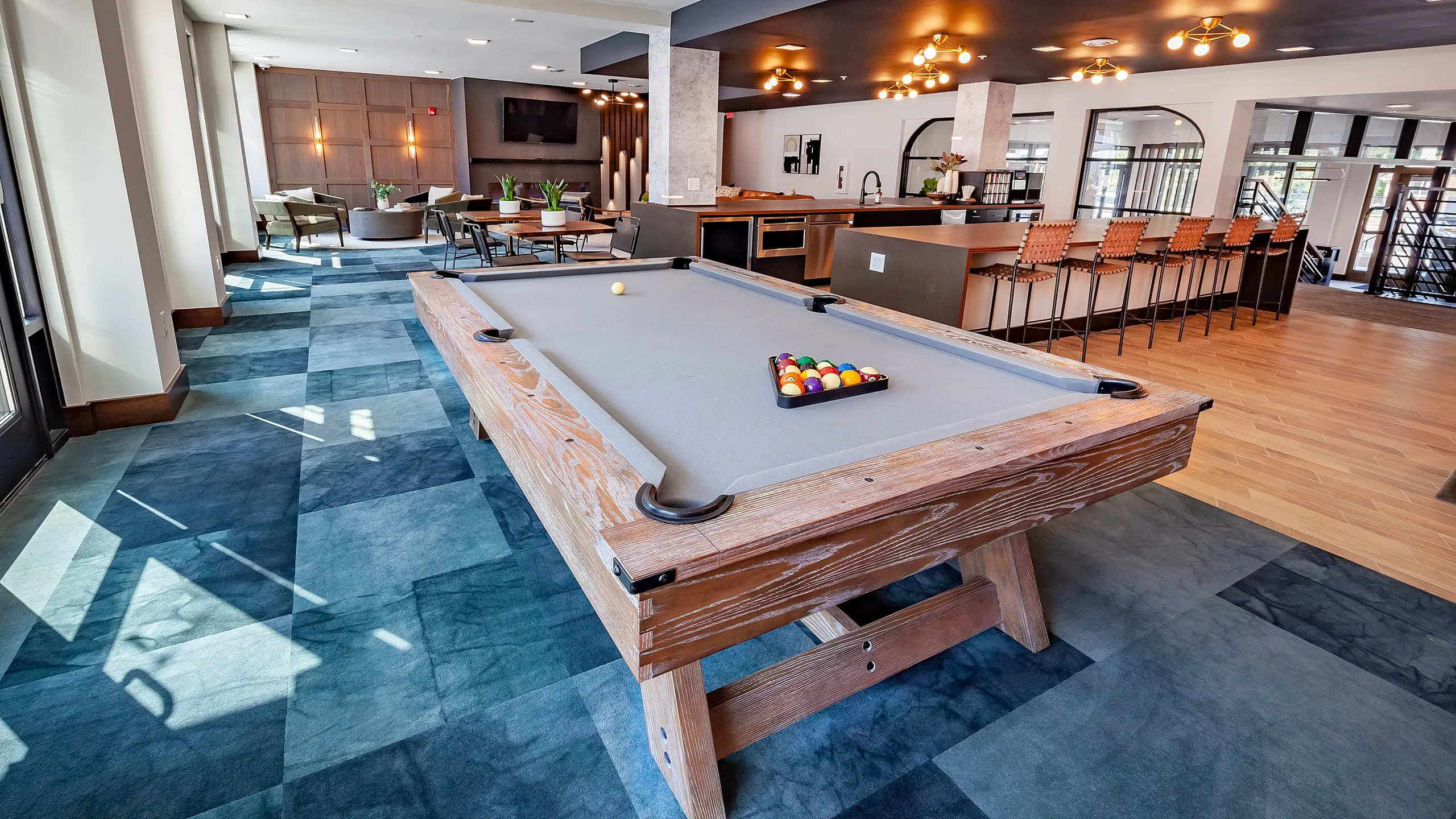 Chic lounge space featuring a sleek pool table, modern kitchen area with stylish bar seating, and inviting seating arrangement under warm ambient lighting.
