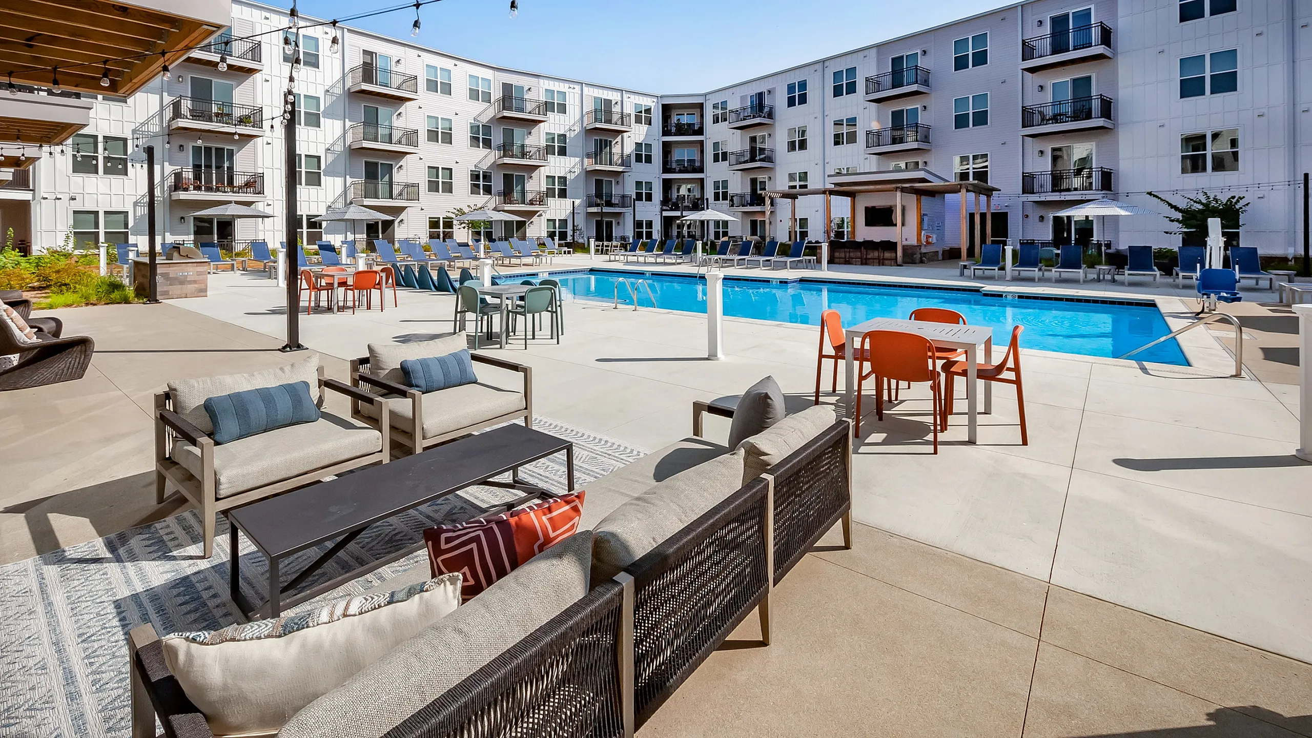 Chic apartment complex featuring a stunning outdoor pool area with modern lounge seating, vibrant patio decor, and spacious balconies.