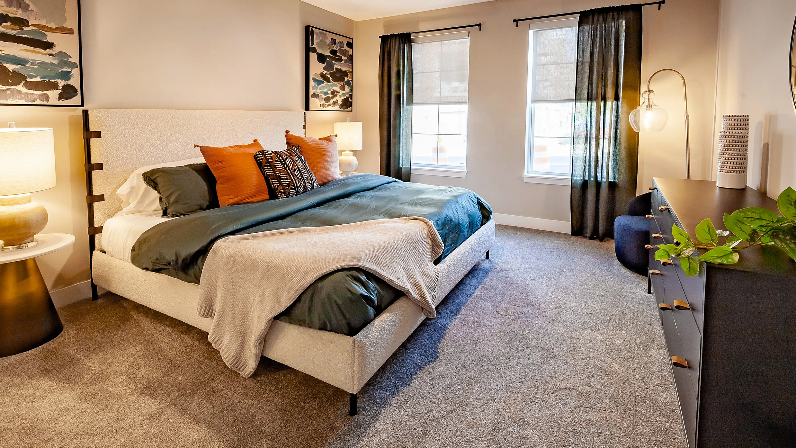 Inviting bedroom with modern decor, featuring a plush bed, stylish bedside lamps, and vibrant artwork, complemented by natural light from large windows.