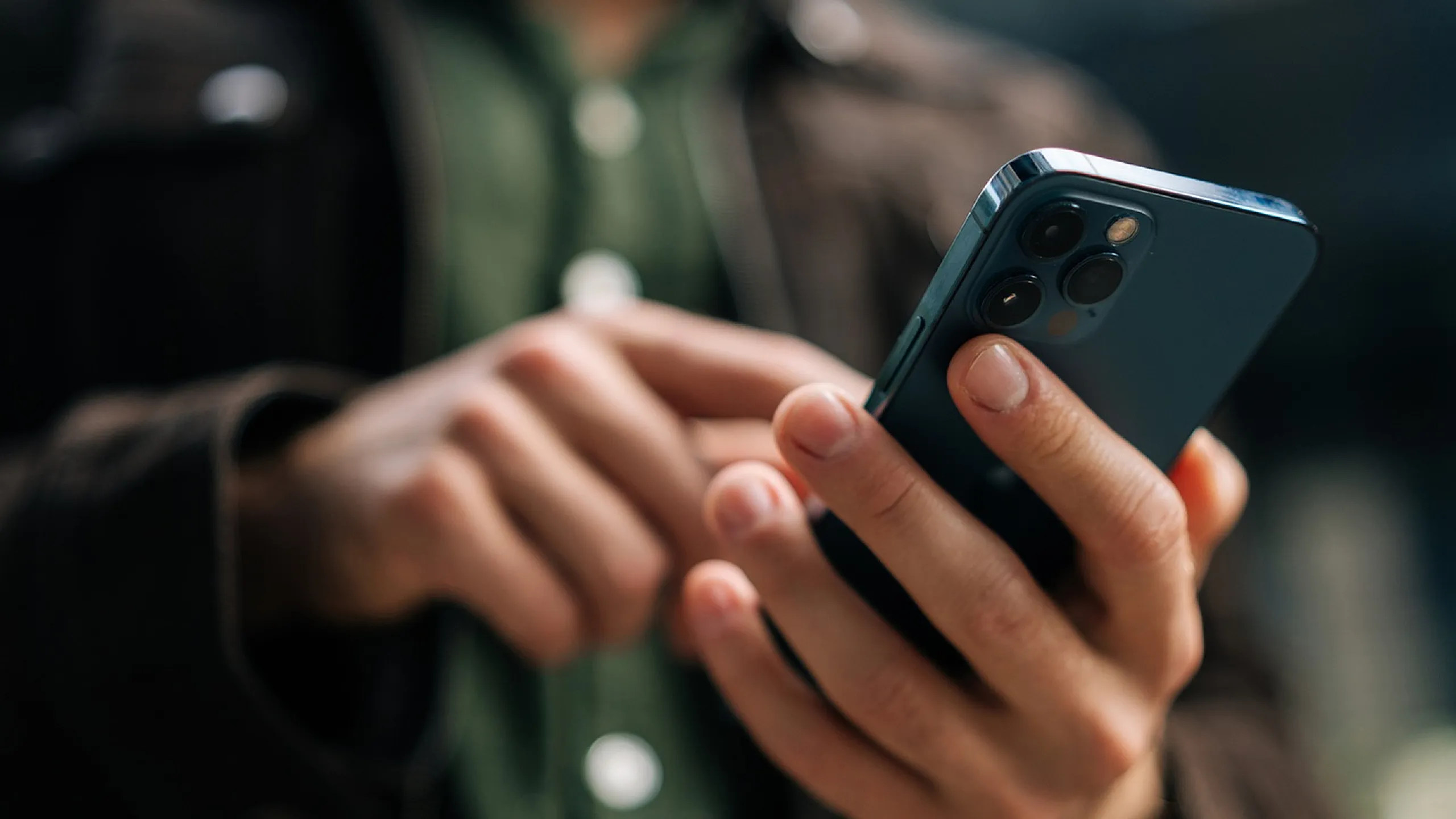 Close-up of a person stylishly dressed, engaging with a modern smartphone.