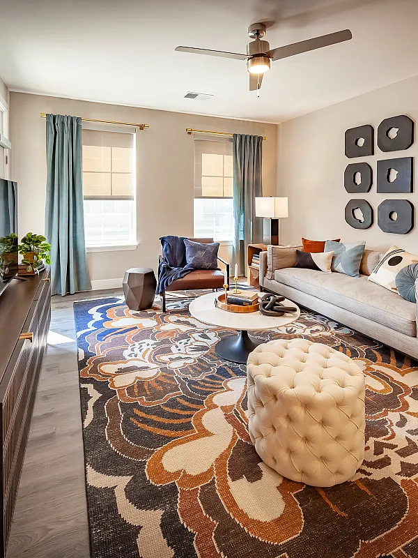 Modern living room with elegant decor, featuring a cozy beige sofa, stylish wall art, and a vibrant patterned rug, bathed in natural light.