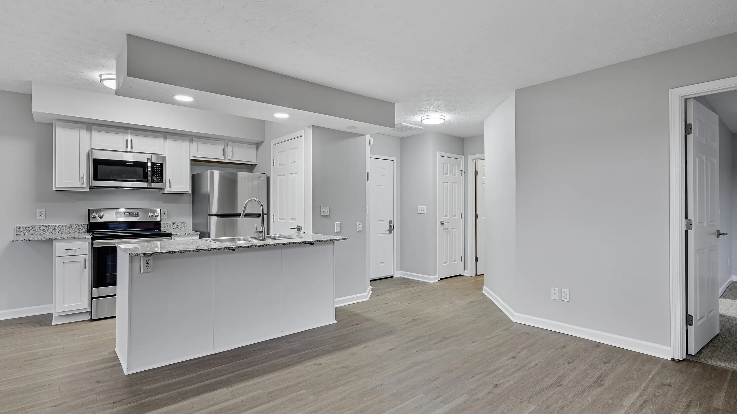 Contemporary open-concept living space with stylish kitchen featuring stainless steel appliances, elegant wood flooring, and modern finishes.