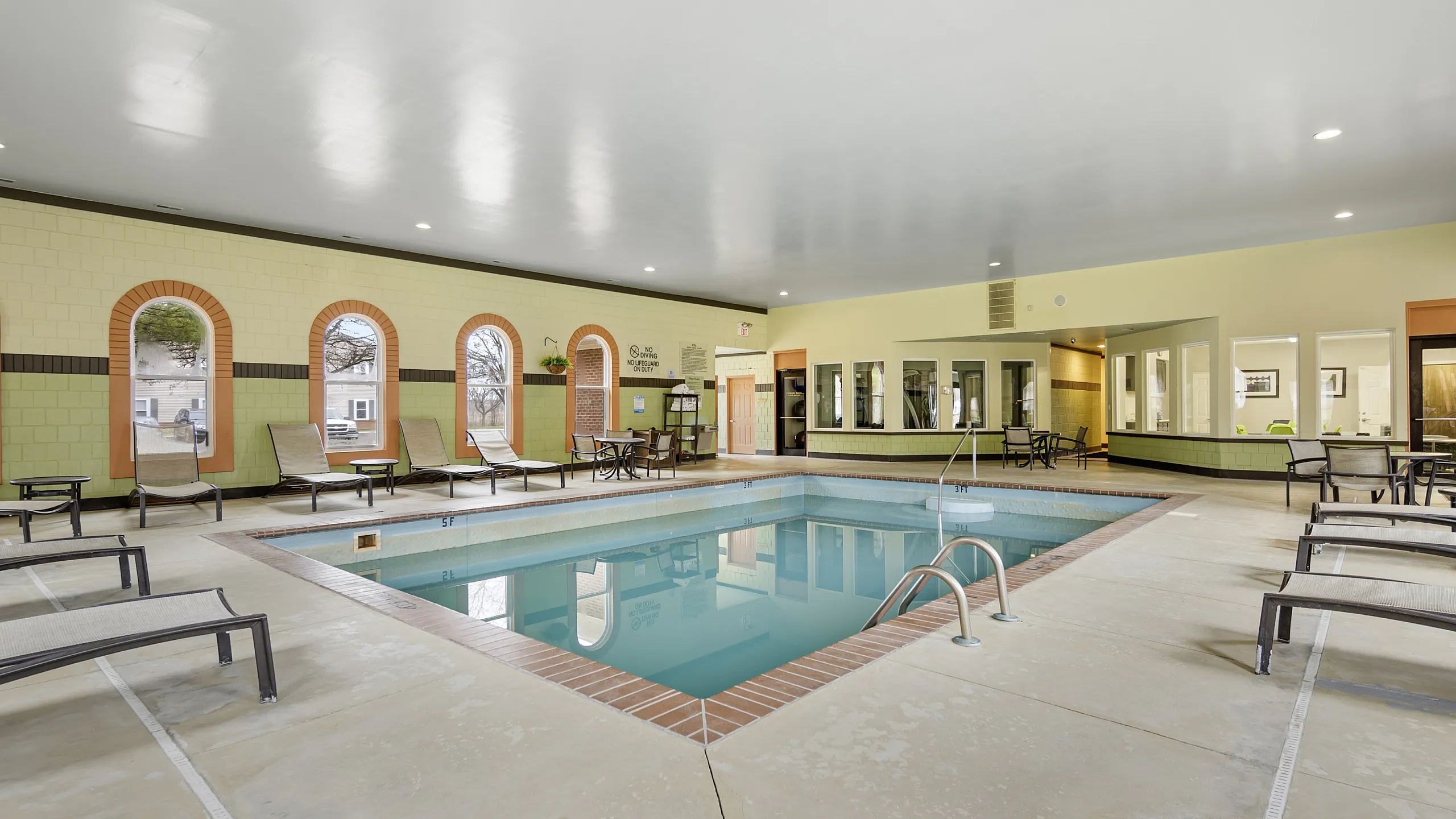 Inviting indoor swimming pool with elegant lounge chairs, surrounded by arched windows offering a serene getaway within a luxurious complex.