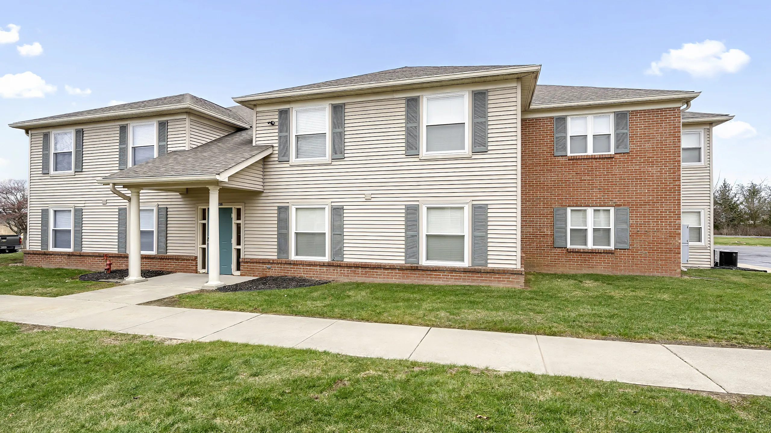 Charming two-story apartment building with brick and siding exterior, surrounded by lush green lawn and spacious sidewalks.