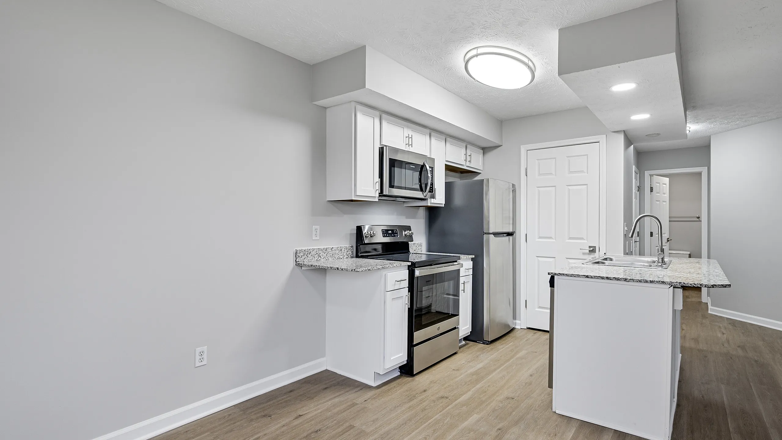 Modern kitchen with sleek stainless steel appliances, elegant white cabinetry, and a chic granite-topped island, set against stylish hardwood floors.