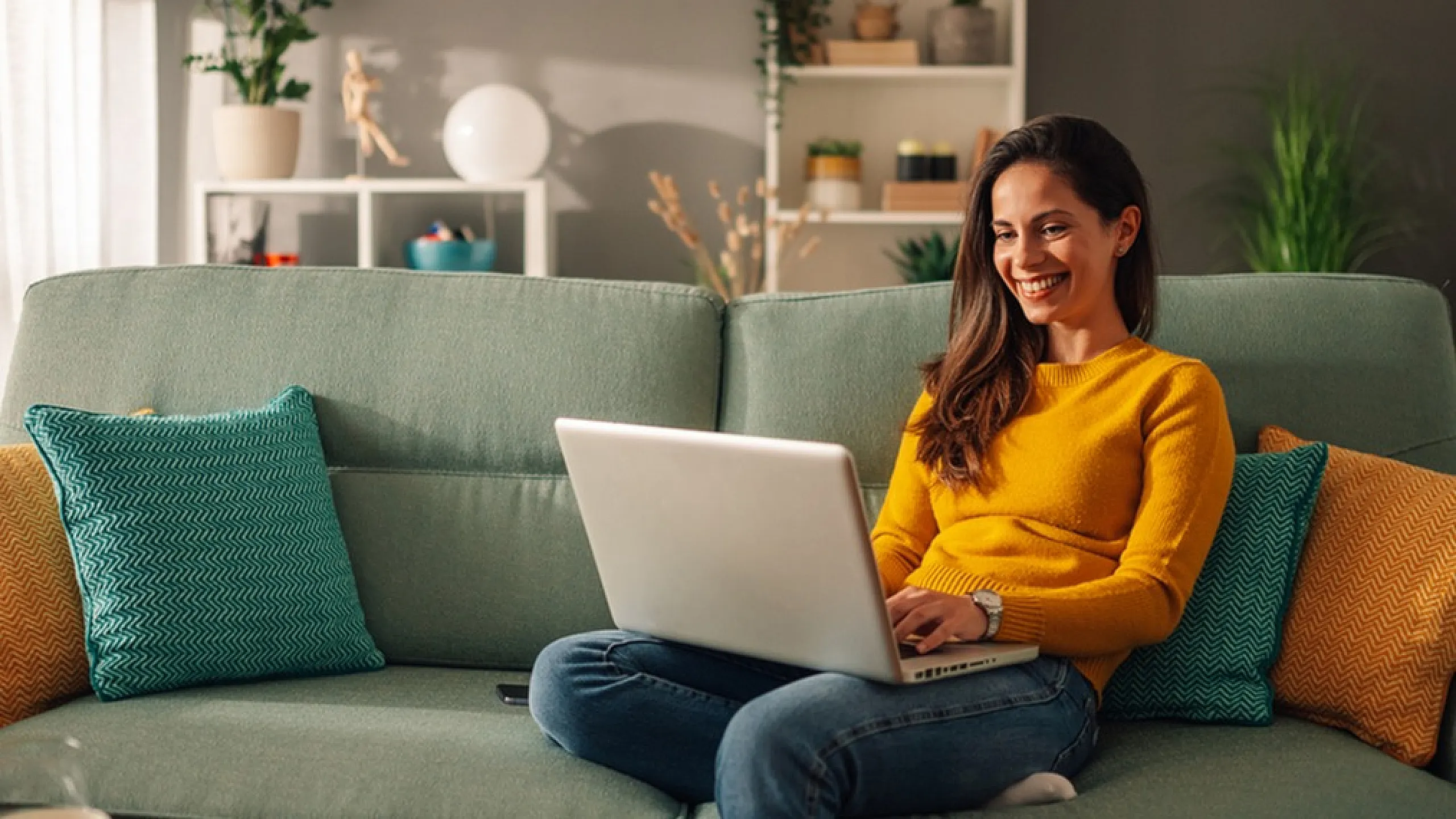 Cozy living room with soft lighting, a comfortable green sofa adorned with colorful cushions, and a person enjoying a laptop, creating a warm and inviting atmosphere.