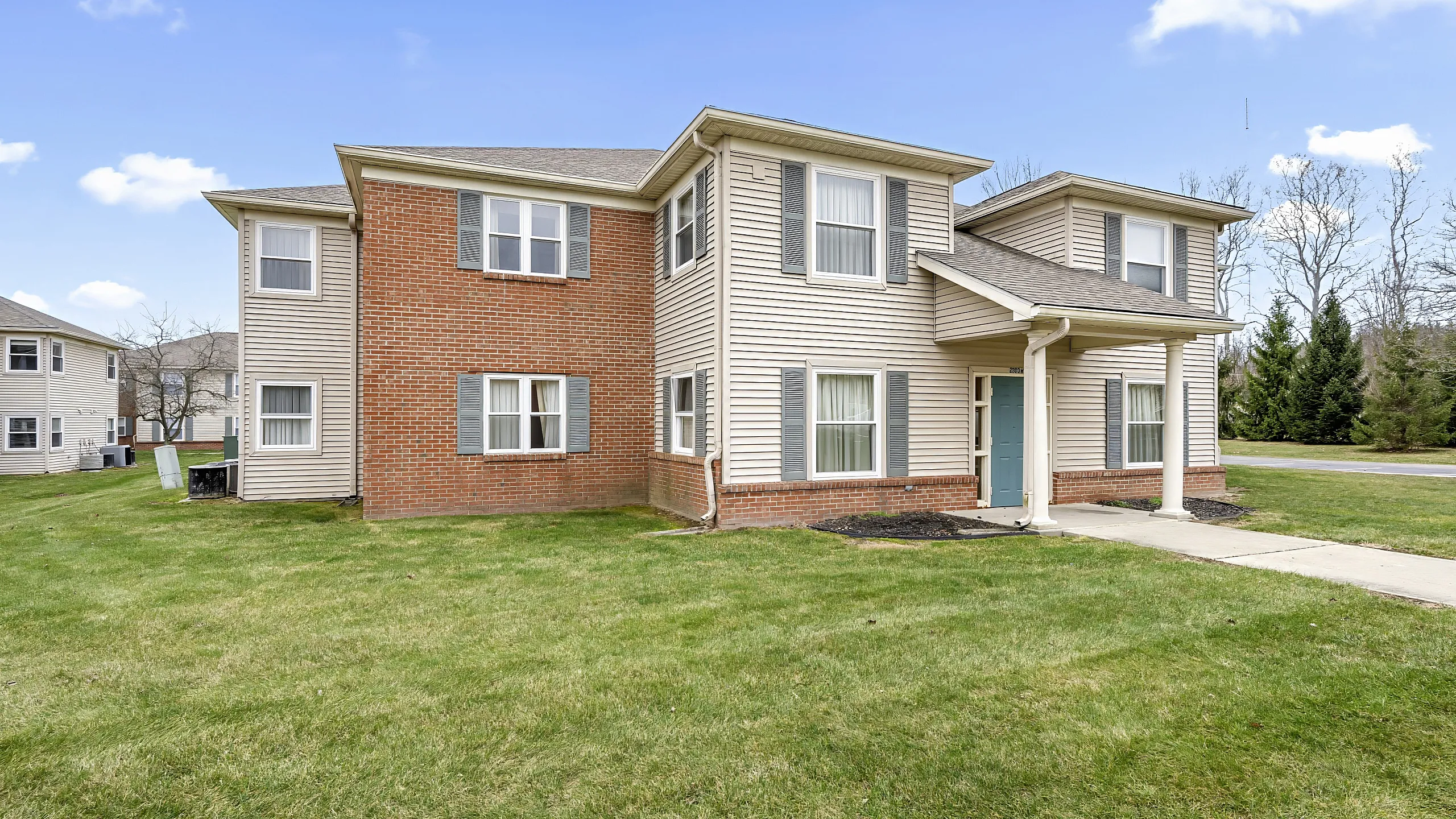 Charming two-story apartment building with brick and siding facade, lush green lawn, and inviting entrance, perfect for comfortable living.