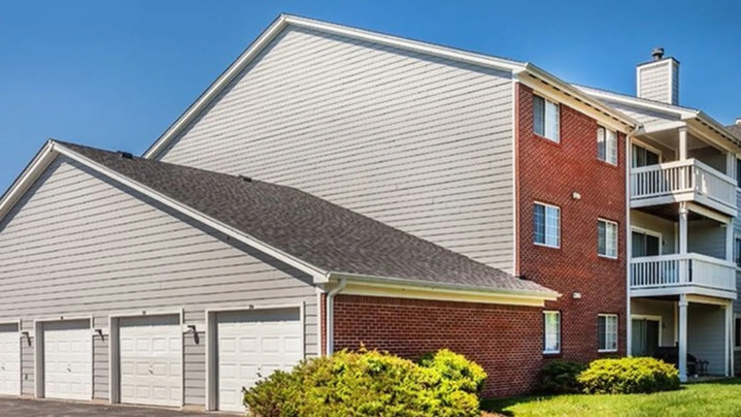 Charming apartment building with brick facade and spacious balconies, alongside a row of convenient garages surrounded by lush greenery.