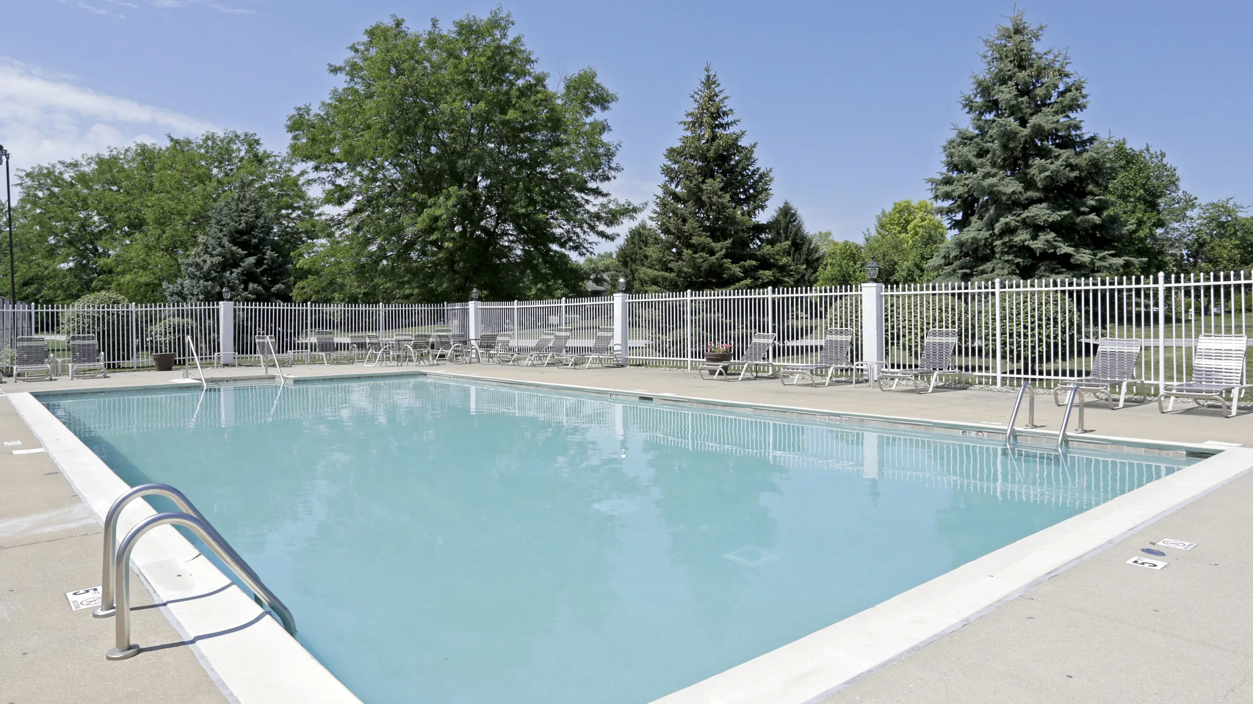 Inviting outdoor swimming pool with crystal-clear water, surrounded by loungers and lush greenery, offering a perfect relaxation spot under blue skies.