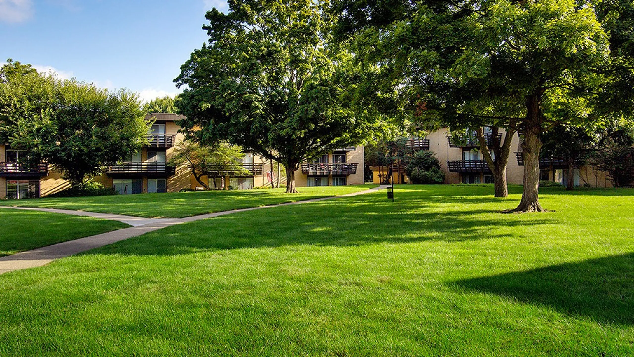 Charming apartment building surrounded by lush green lawns and mature trees, offering a tranquil and inviting atmosphere.