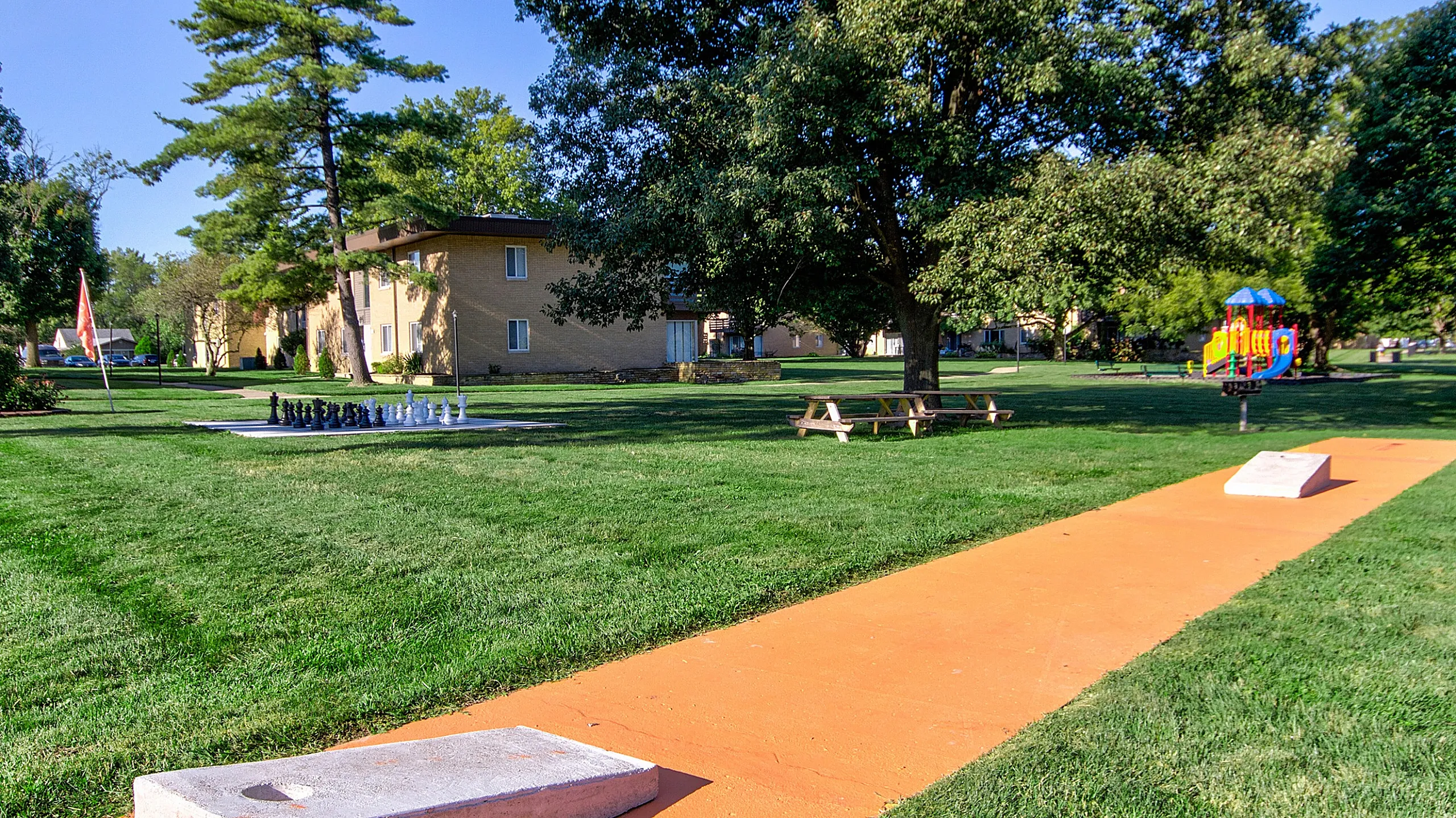 Inviting outdoor area featuring lush green lawns, a large chess set, and a vibrant playground, perfect for family leisure and relaxation.