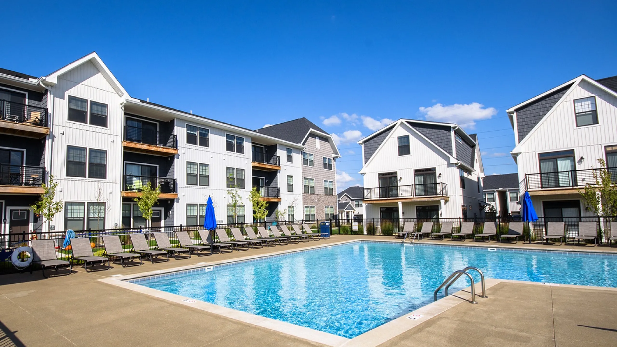 Luxurious apartment complex with modern architectural design featuring a sparkling outdoor pool and ample sun loungers for relaxation under blue skies.