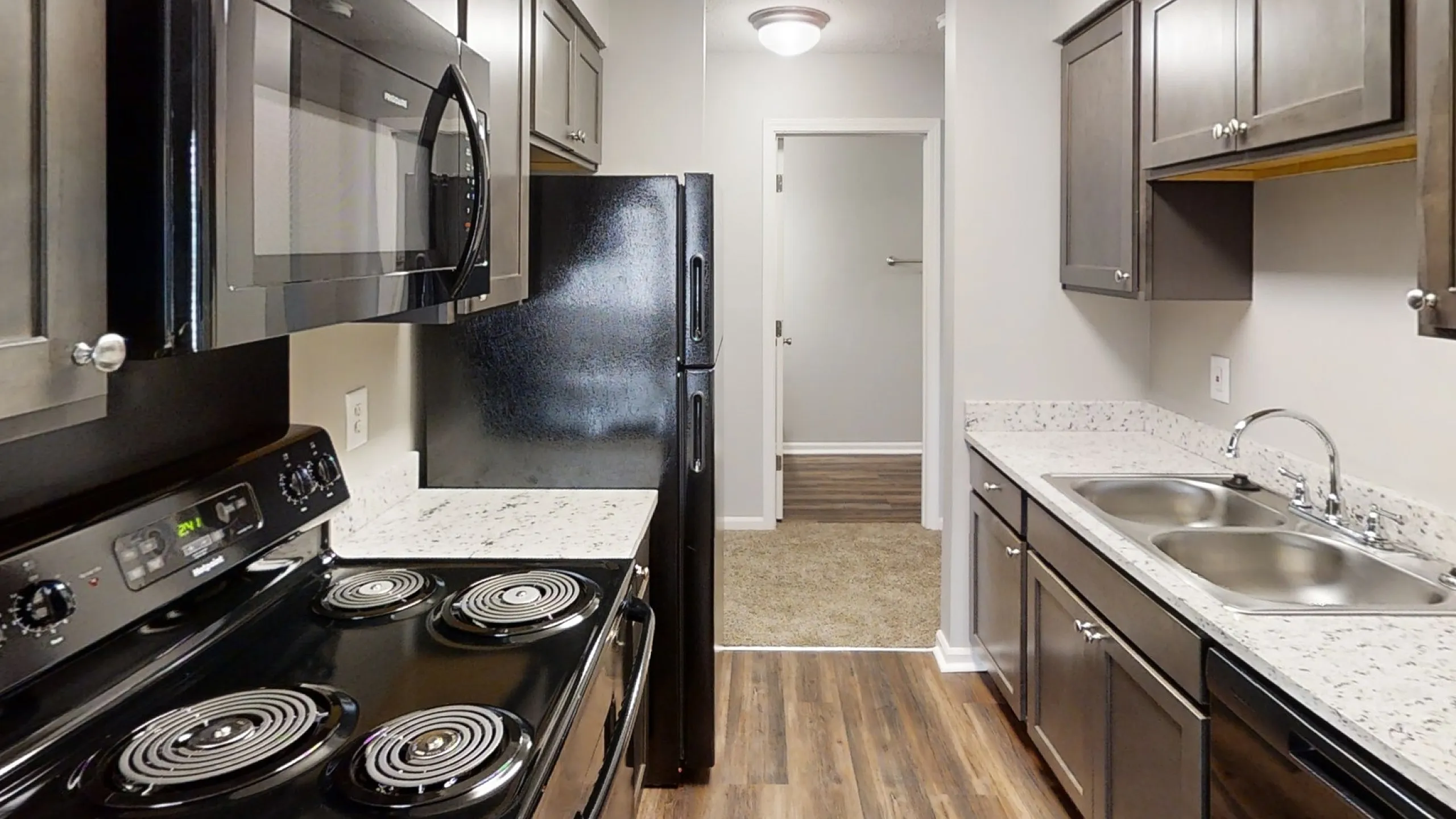 Modern kitchen with sleek black appliances, granite countertops, and elegant dark cabinets on hardwood flooring.