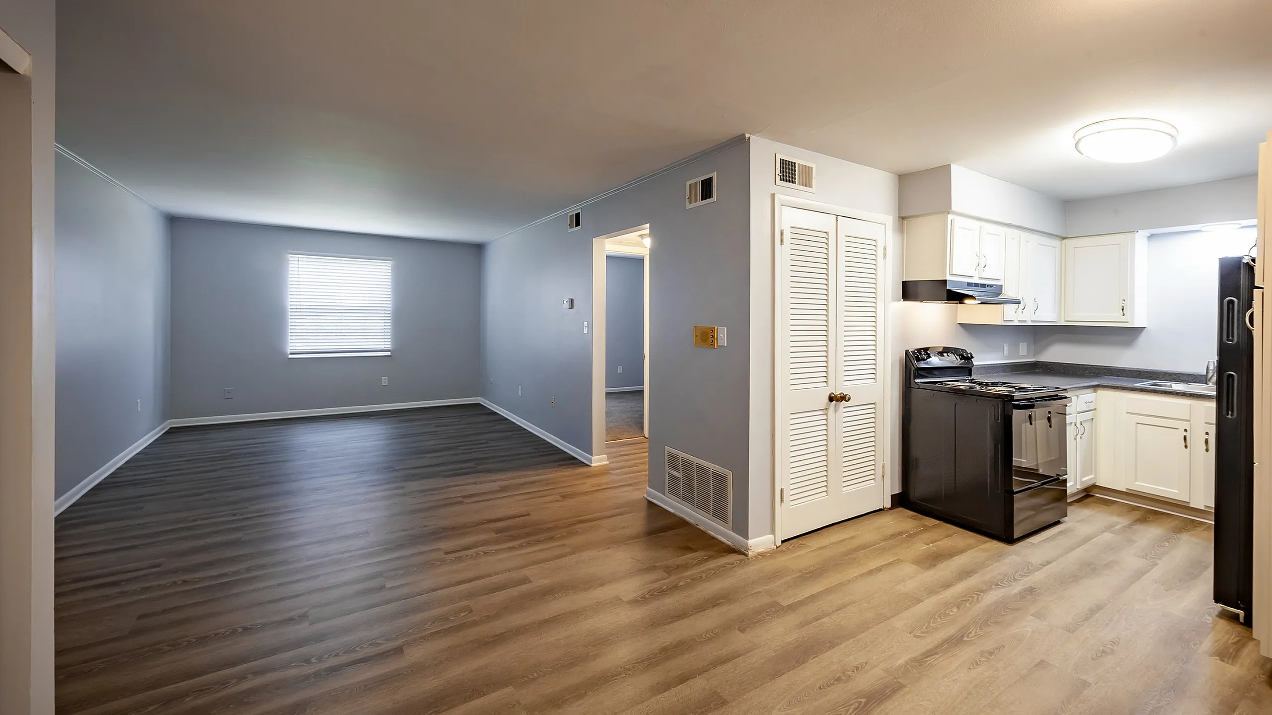 Chic open-plan apartment with elegant hardwood floors, featuring a cozy kitchen, spacious living area, and ample natural light from a large window.