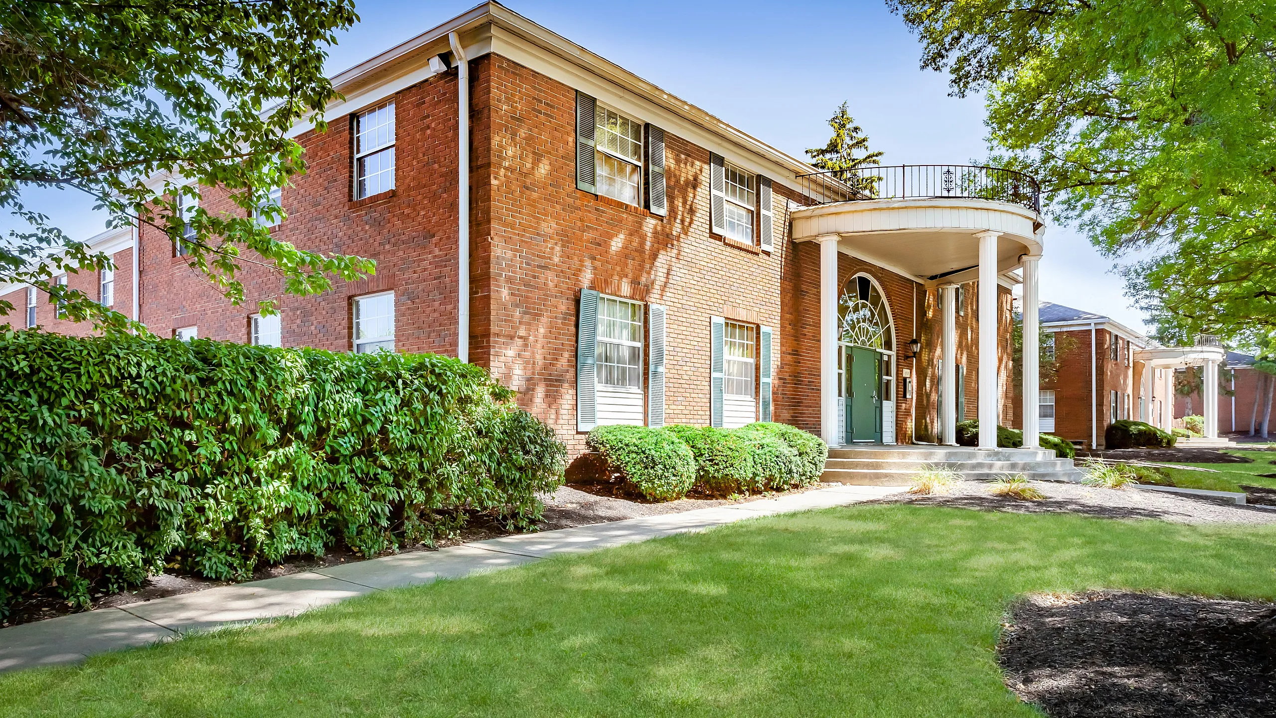 Charming brick apartment building with elegant columns and lush greenery creating a welcoming front entrance.