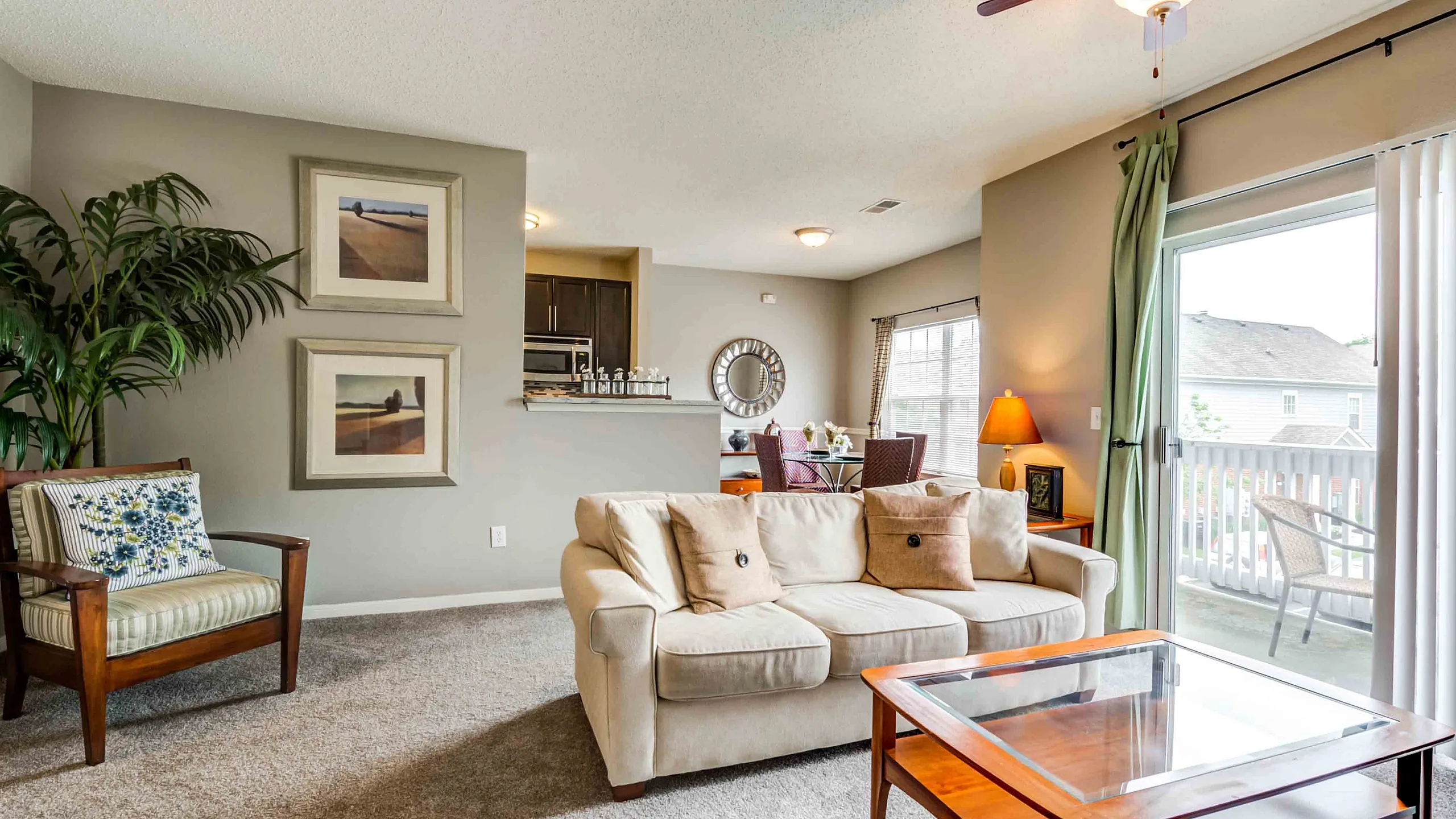 Grande Reserve at Geist-Inviting living space with plush carpeting, elegant decor, and abundant natural light from the balcony, seamlessly connecting to a cozy dining area and modern kitchen.