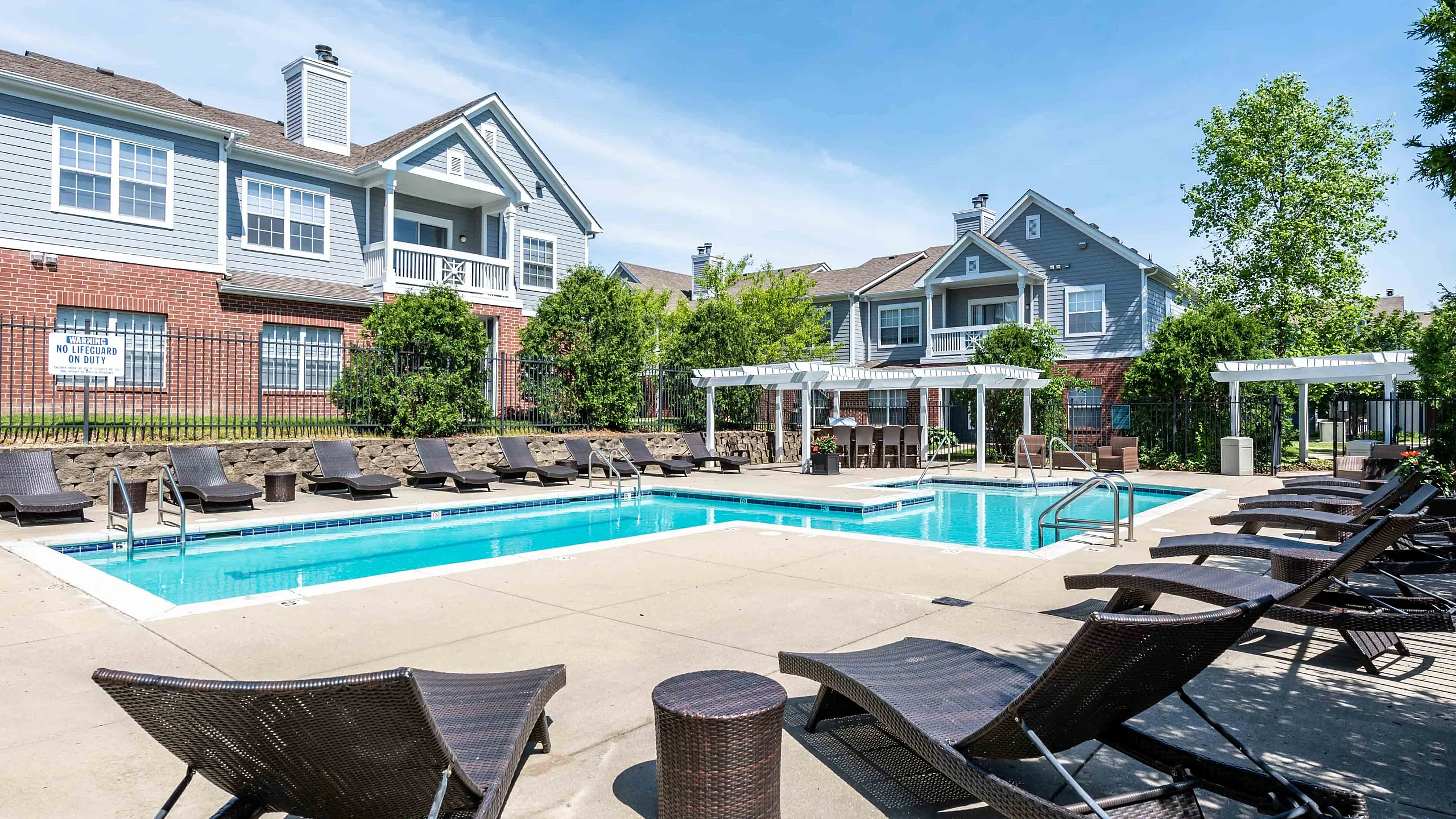 Inviting outdoor pool area with stylish loungers and lush landscaping, set against charming residential buildings. Perfect for relaxation and leisure.