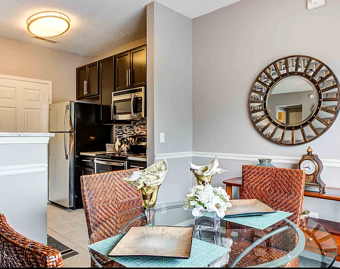 Chic apartment kitchen and dining area featuring modern appliances, elegant wicker chairs, and a stylish round mirror accentuating the contemporary decor.