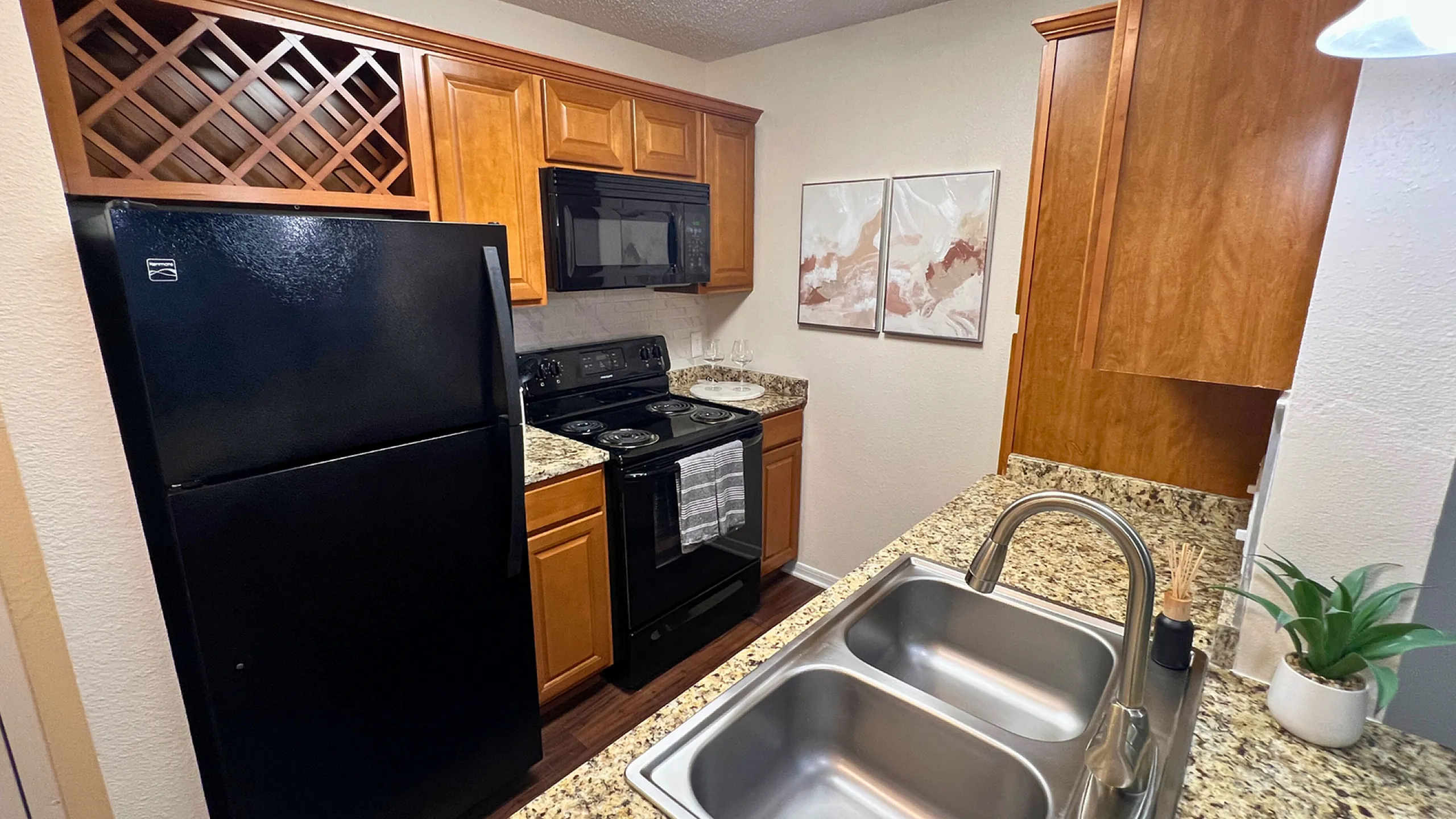 Canal Square Modern kitchen with granite countertops, sleek black appliances, wooden cabinetry, and dual sink, ideal for culinary creativity.