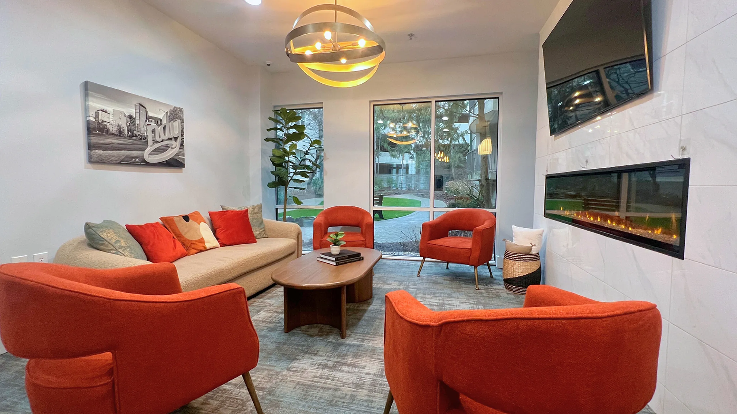Modern and inviting living room with vibrant orange chairs, a cozy beige sofa, and a sleek wall-mounted fireplace, perfect for relaxation.