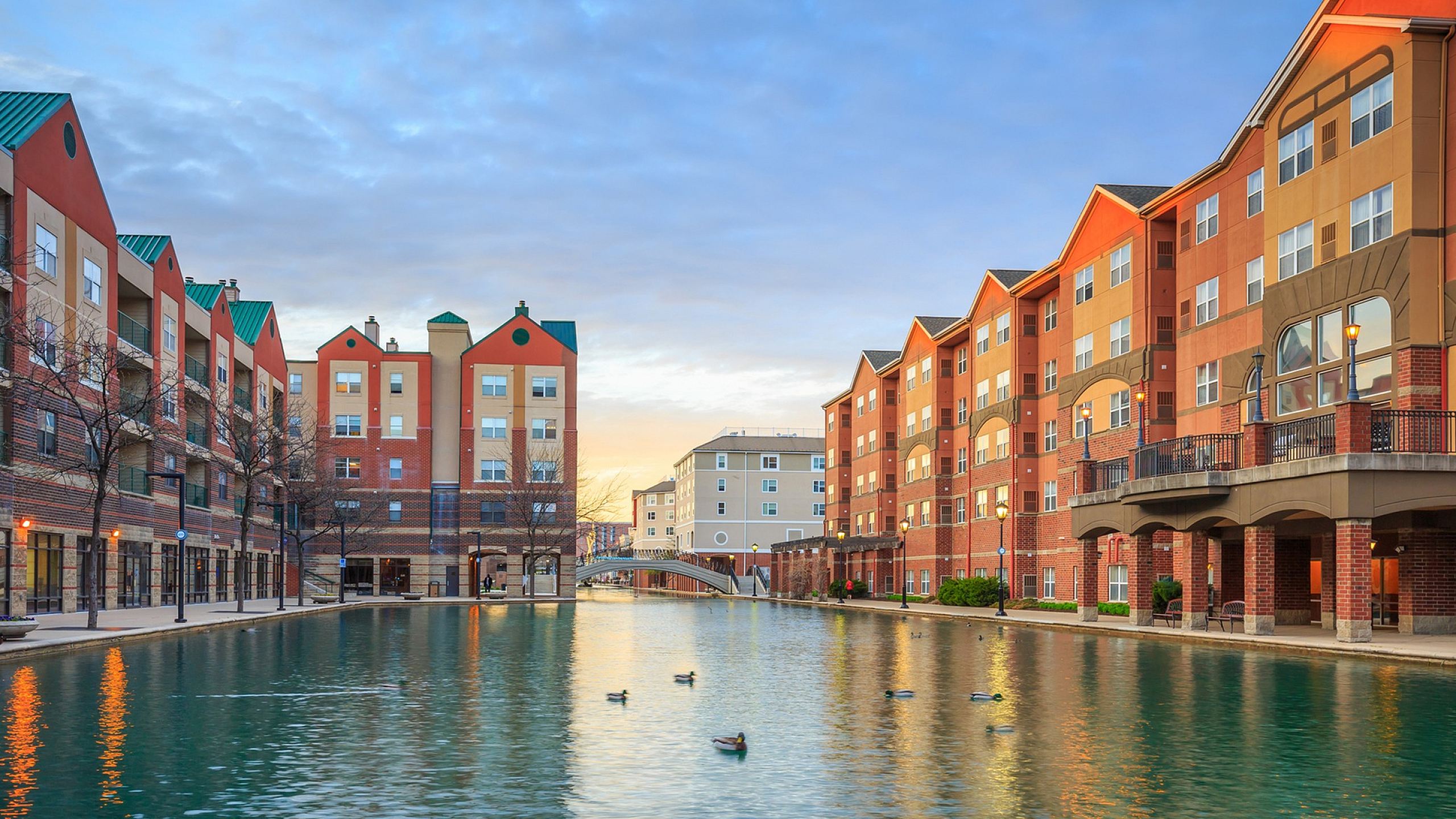 Charming waterfront apartment complex with vibrant architecture, reflecting in a serene canal at sunset.