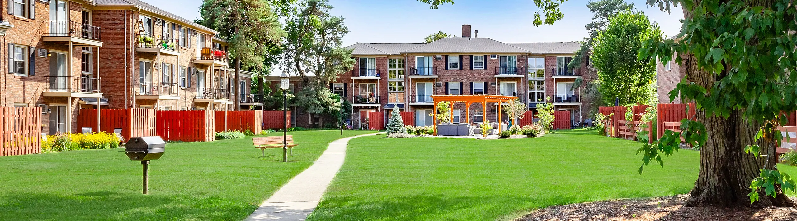 Charming apartment complex with lush green lawns, mature trees, and a picturesque gazebo nestled in a vibrant courtyard.