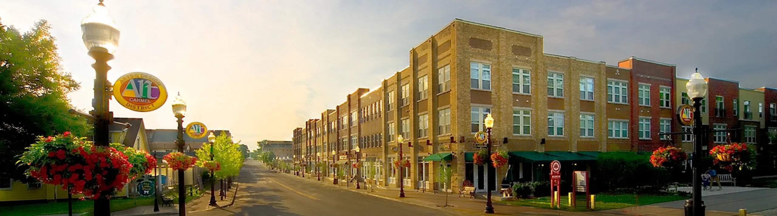 Charming street view in the Arts & Design District with modern apartments, vibrant hanging flower baskets, and welcoming streetlamps.