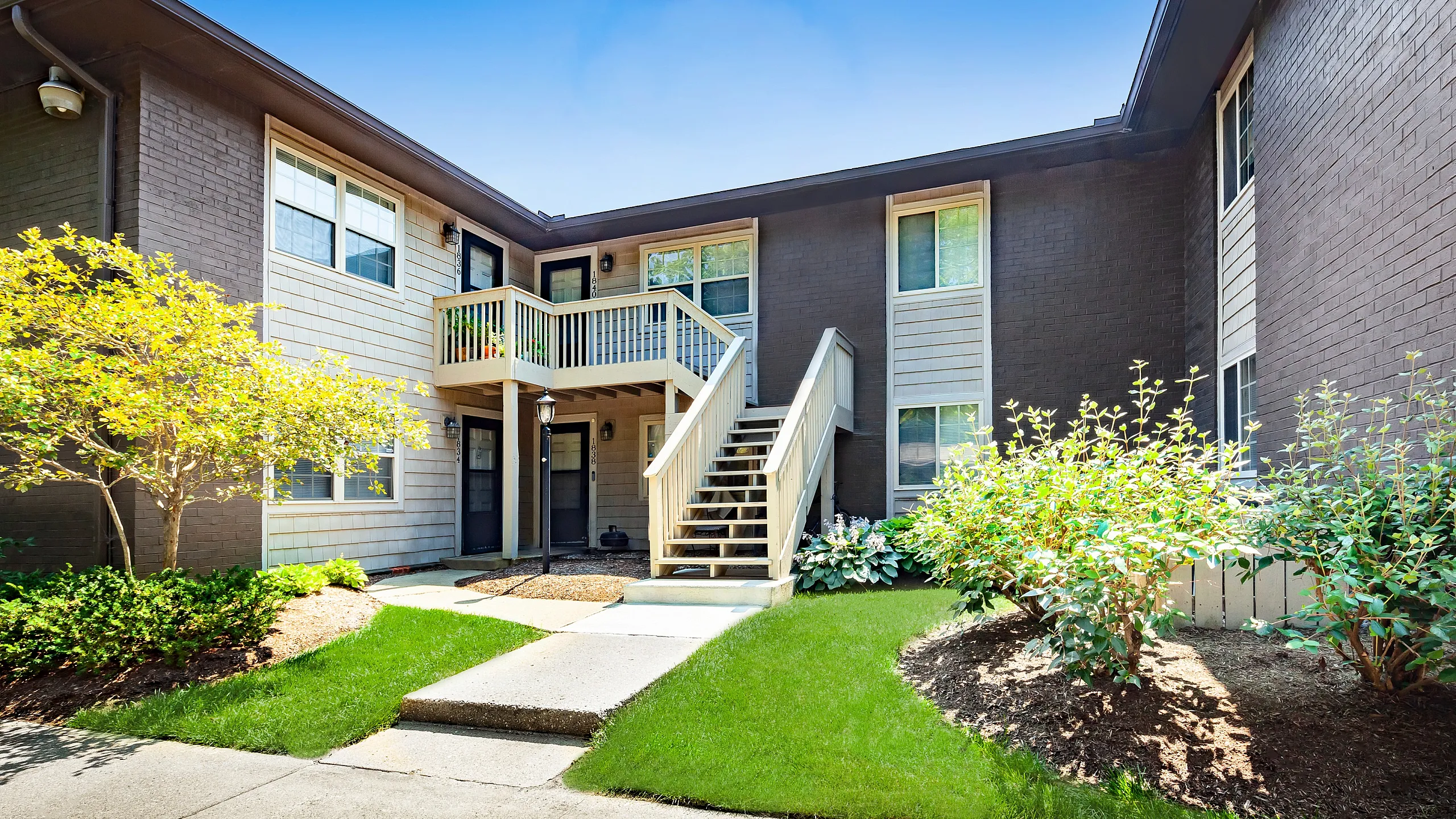 Charming apartment exterior with vibrant landscaping, featuring a welcoming staircase and private balcony, perfect for serene living.