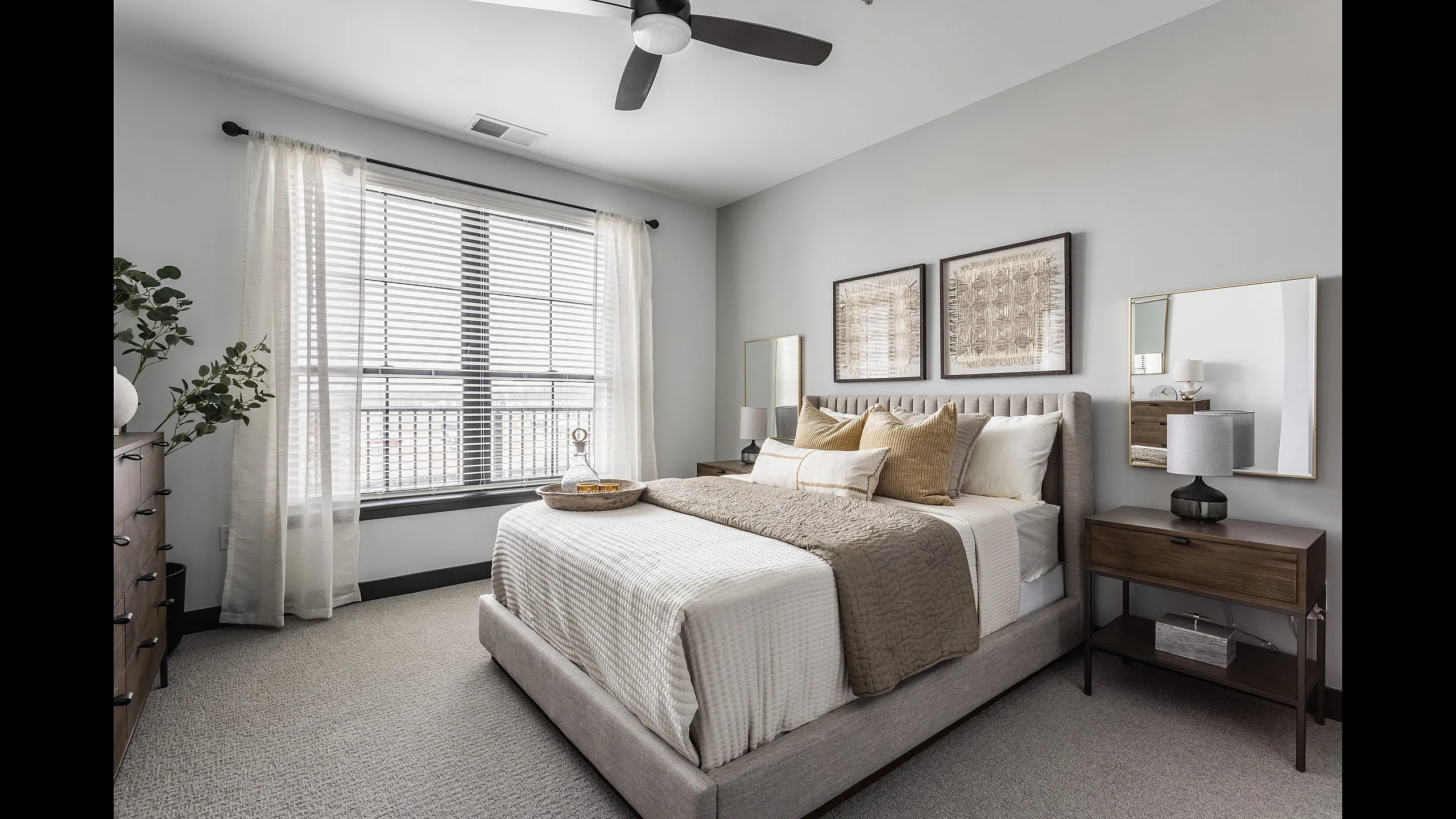 Elegant bedroom with cozy neutral tones, featuring a plush bed, stylish decor, and large sunlit window.