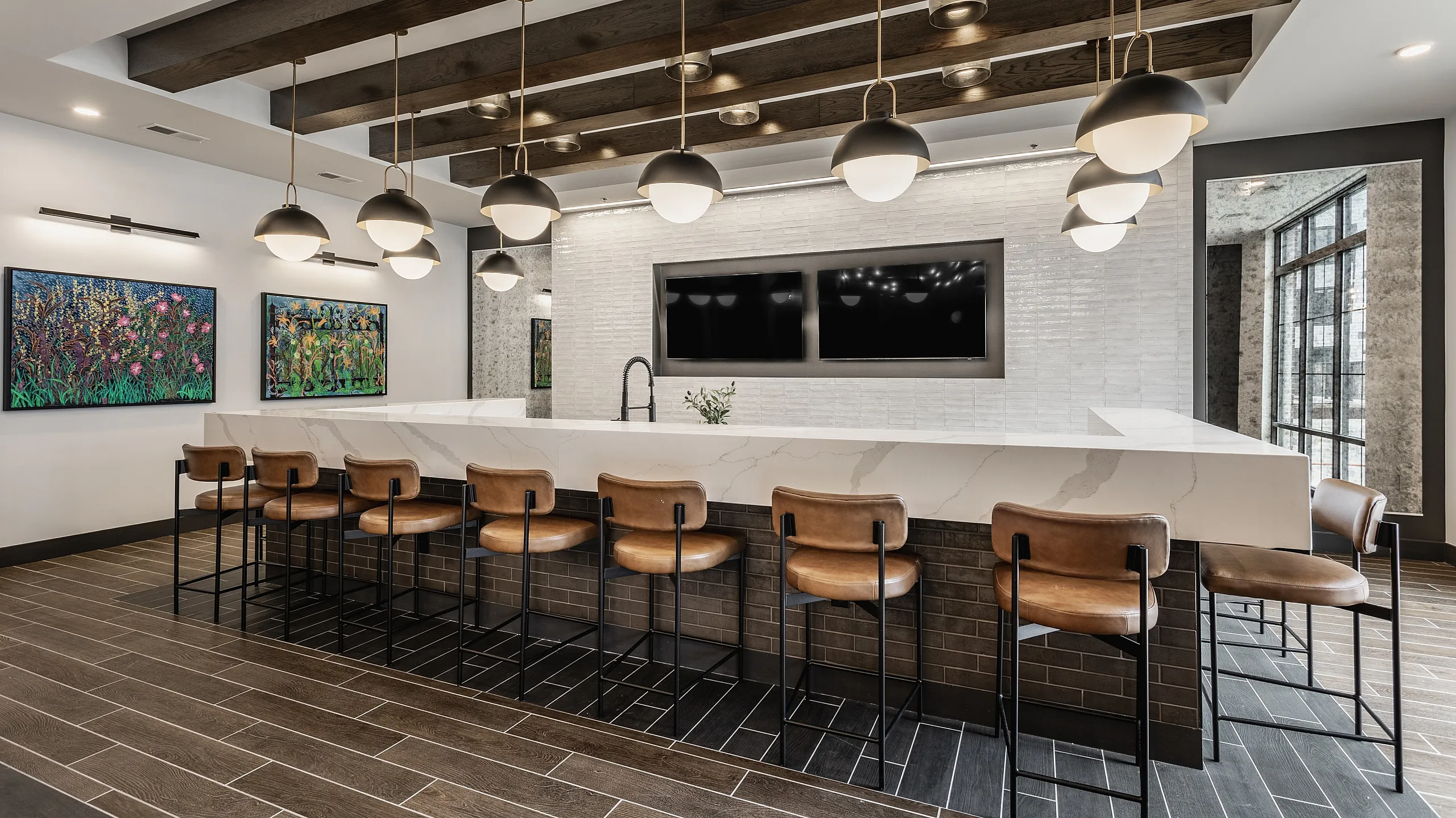 Modern kitchen area boasting a sleek marble island with leather bar stools, chic pendant lighting, and contemporary artwork on the walls.