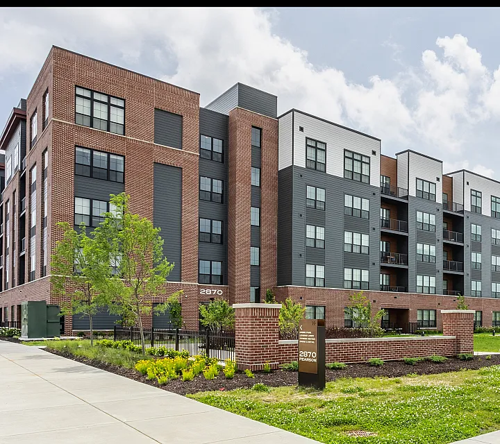 Modern apartment complex with stylish brick and siding facade, surrounded by lush landscaping and inviting sidewalk paths.