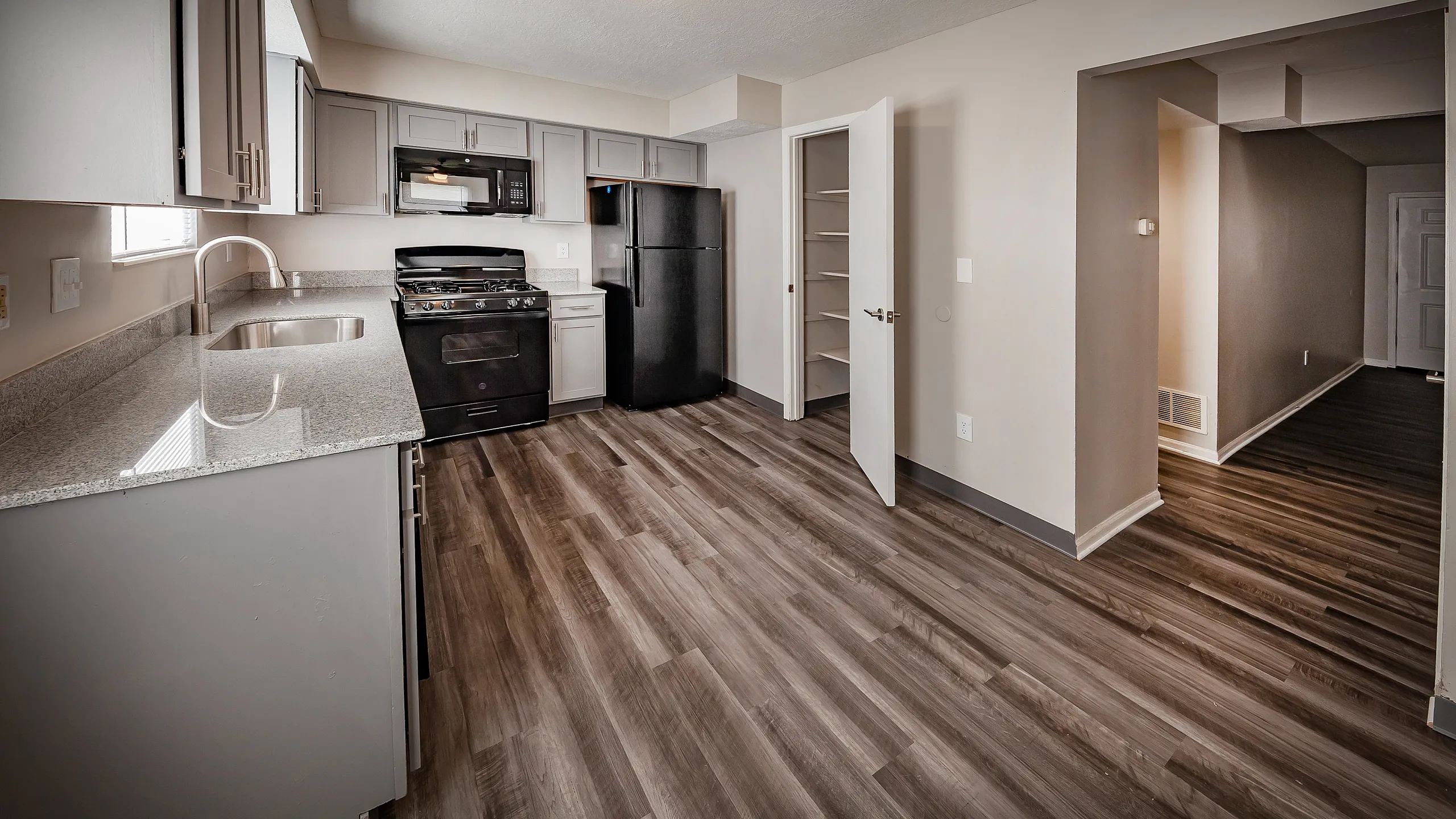 Modern kitchen with sleek grey cabinetry, granite countertops, and rich wood floors, featuring a pantry and state-of-the-art black appliances.