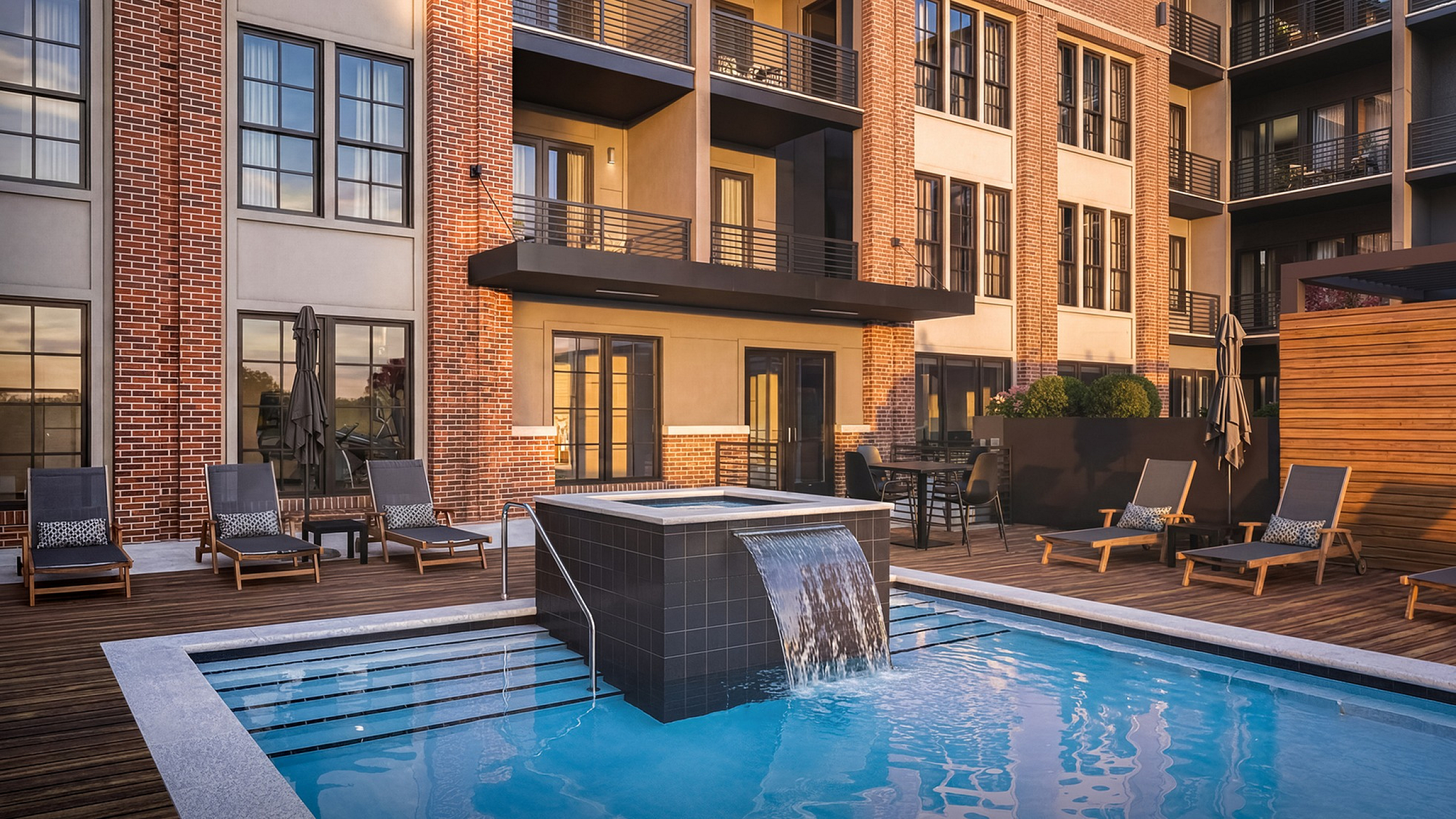 Luxurious apartment complex with a modern pool and relaxing sun loungers, surrounded by elegant brick architecture and inviting outdoor spaces.