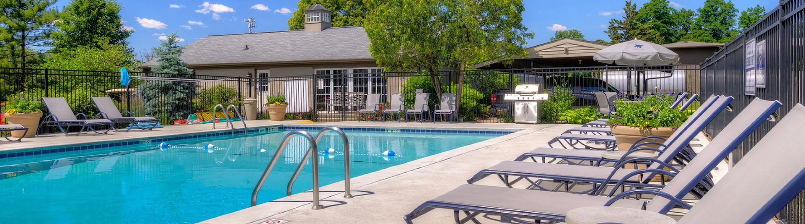 Luxurious outdoor pool area with comfortable loungers and vibrant greenery under a clear blue sky, offering a perfect relaxation retreat.