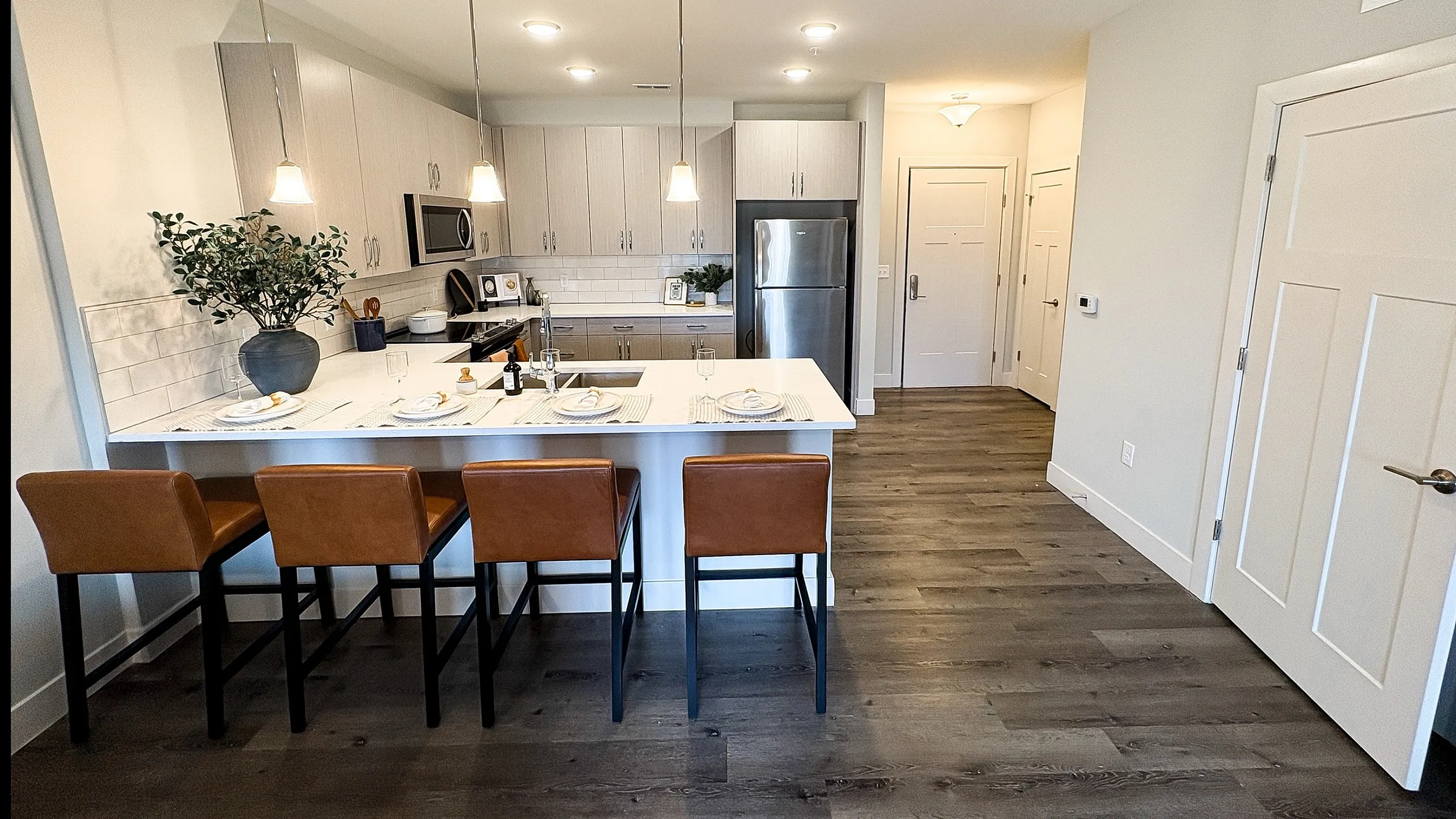 Chic modern kitchen with sleek cabinetry, stainless steel appliances, and stylish pendant lighting over a breakfast bar with four leather stools.