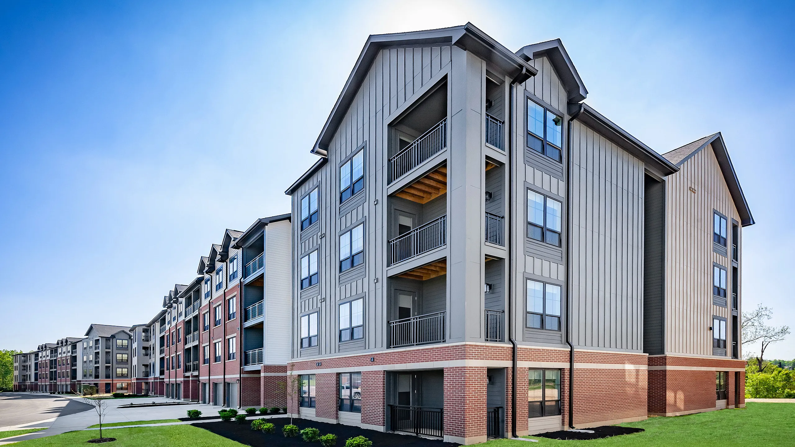 Modern four-story apartment complex showcasing stylish architecture, expansive balconies, and well-maintained landscaping under a clear blue sky.