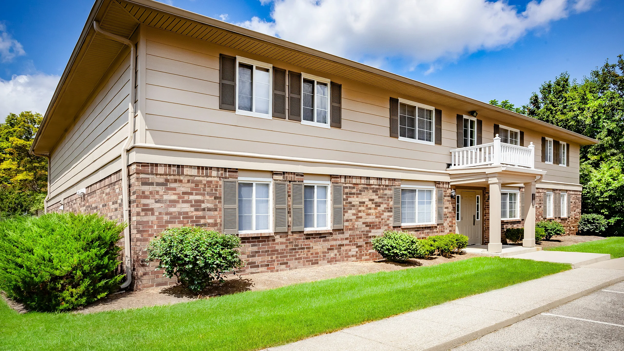 Charming two-story apartment complex with classic brick and siding exterior, surrounded by lush greenery and a bright, inviting atmosphere.