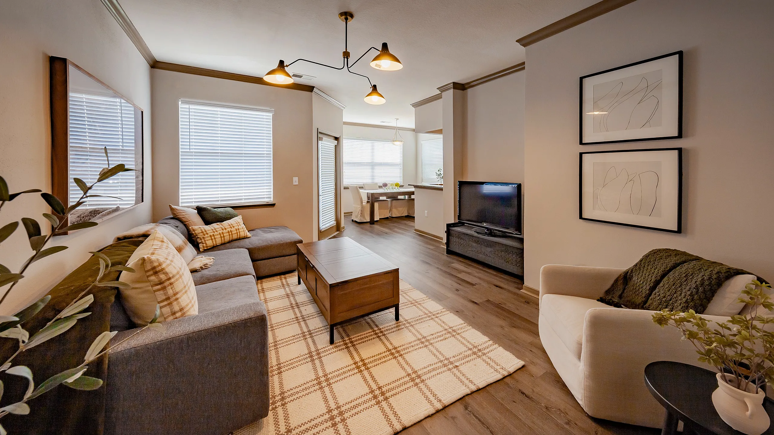 Inviting living room boasting a cozy gray sectional, elegant lighting, and stylish decor with natural light streaming through large windows at River Ridge Apartments