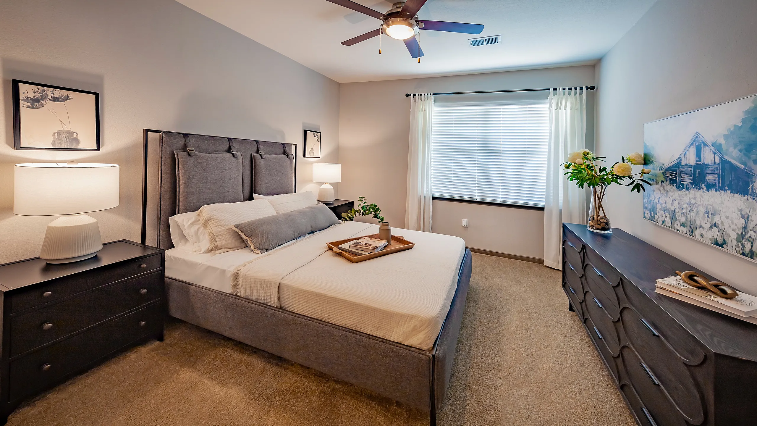 Charming bedroom with a plush bed, modern ceiling fan, and decorative lamps, perfect for relaxation. A large window allows natural light to fill the space.