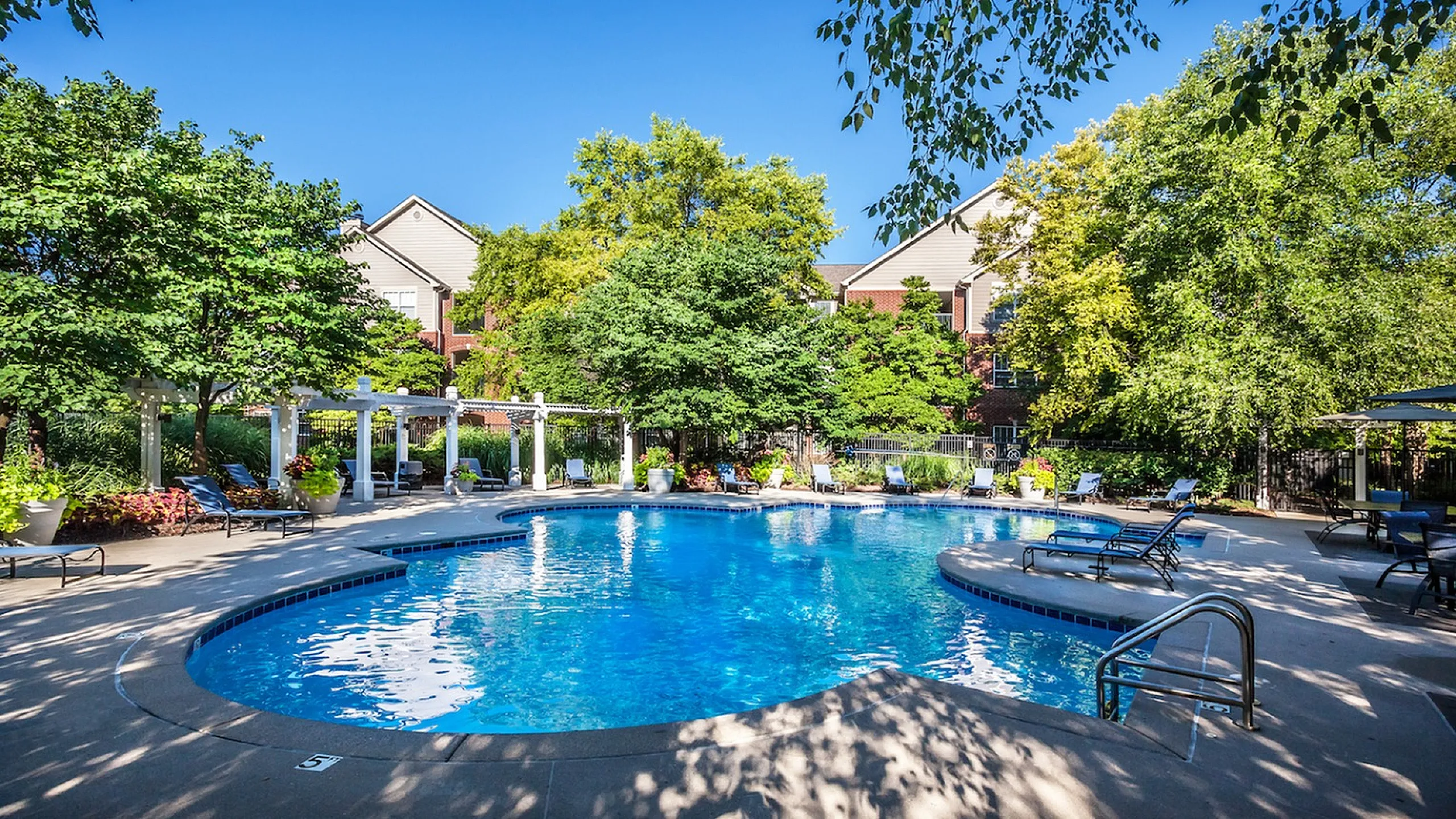 Inviting outdoor pool area surrounded by lush greenery, featuring comfortable lounge chairs and a serene atmosphere.