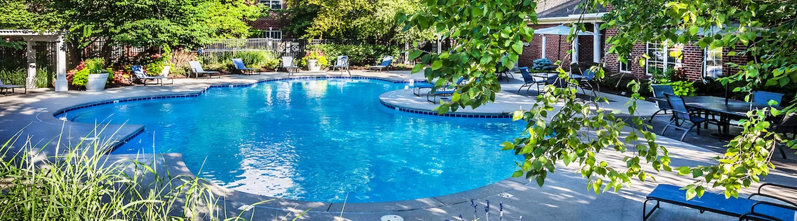 Luxurious apartment complex featuring a shimmering swimming pool surrounded by lush greenery and relaxing lounge chairs.