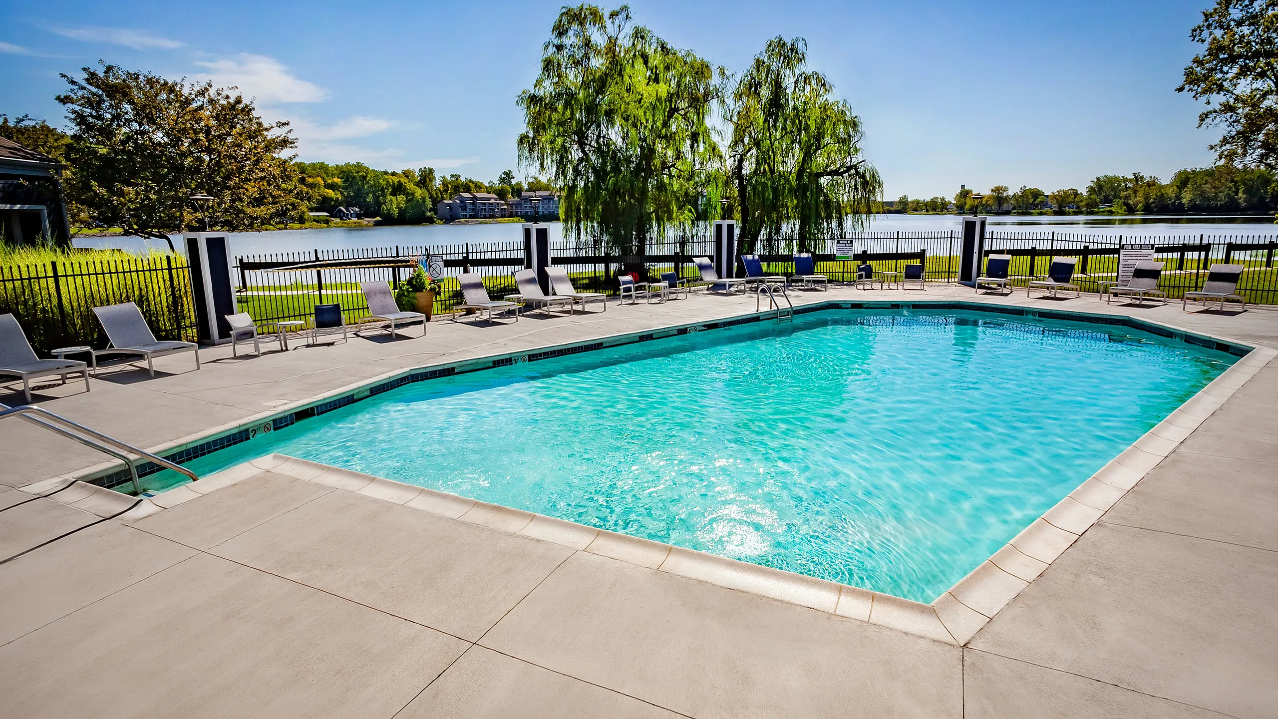 Inviting outdoor pool area with sparkling blue water, surrounded by elegant lounge chairs and a scenic lake view, perfect for relaxation.