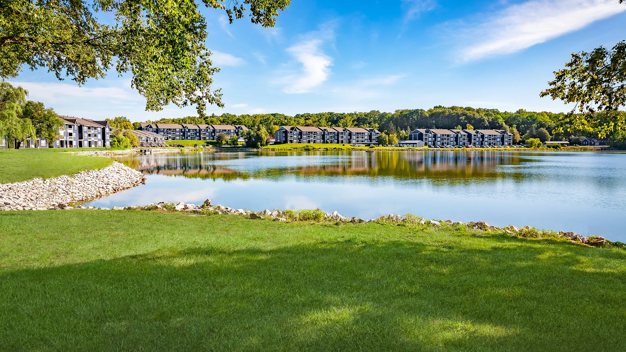 Charming lakeside apartment community with scenic views, surrounded by lush greenery and a serene water feature.
