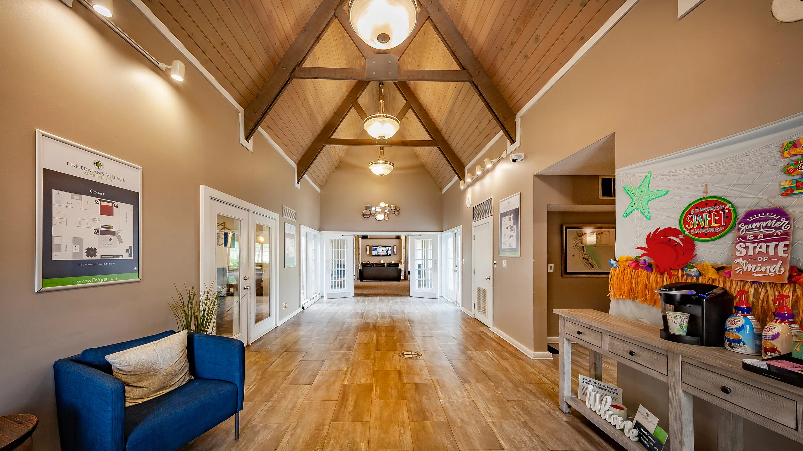 Inviting apartment lobby with high ceilings, elegant lighting, and cozy seating, leading to double glass doors.