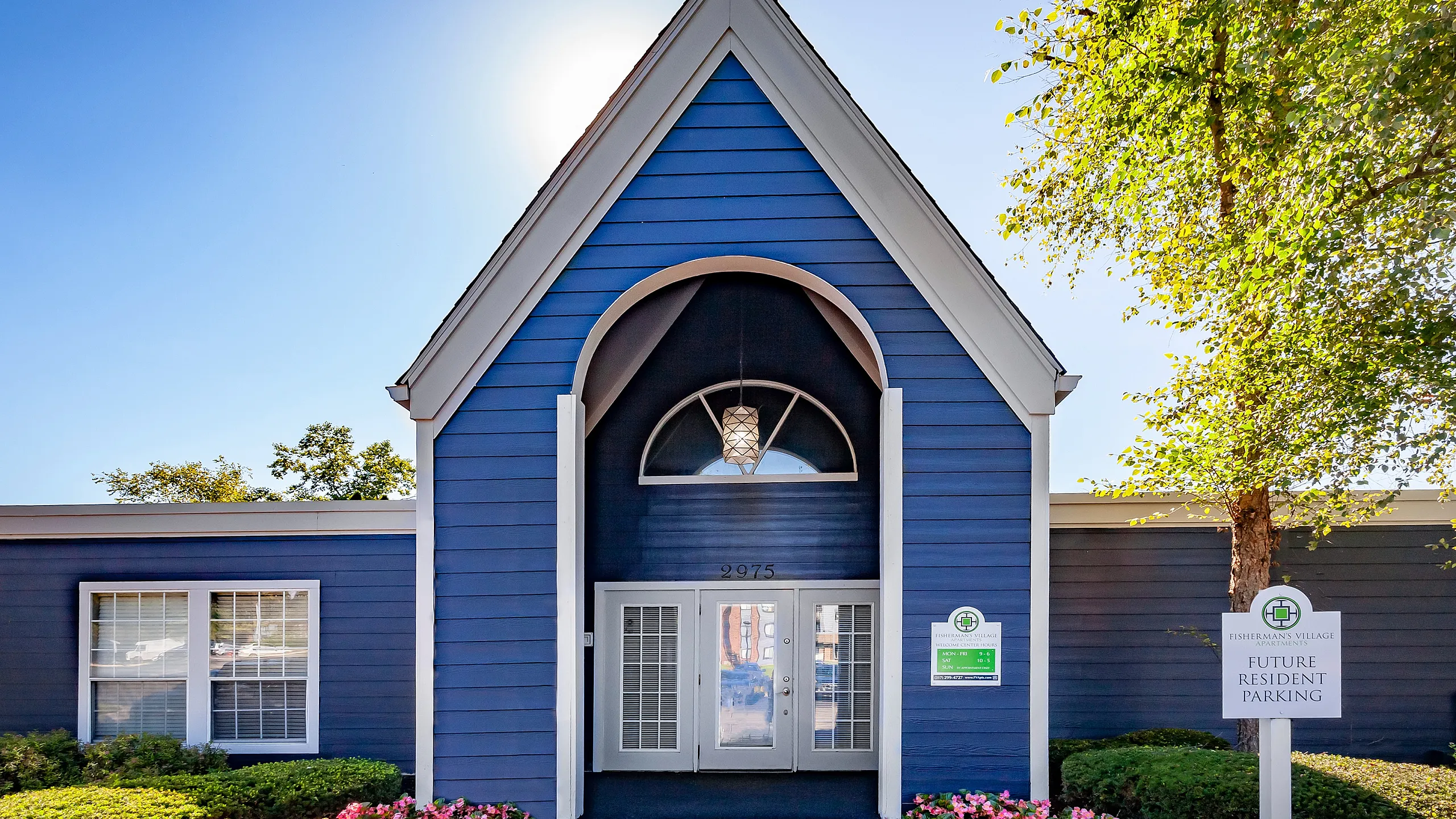 Charming apartment entrance with vibrant blue siding, elegant archway, and blooming flowerbed, symbolizing a welcoming and picturesque residential community.
