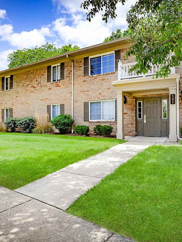 Charming brick apartment building with lush green lawns and large windows, offering a tranquil and inviting atmosphere.