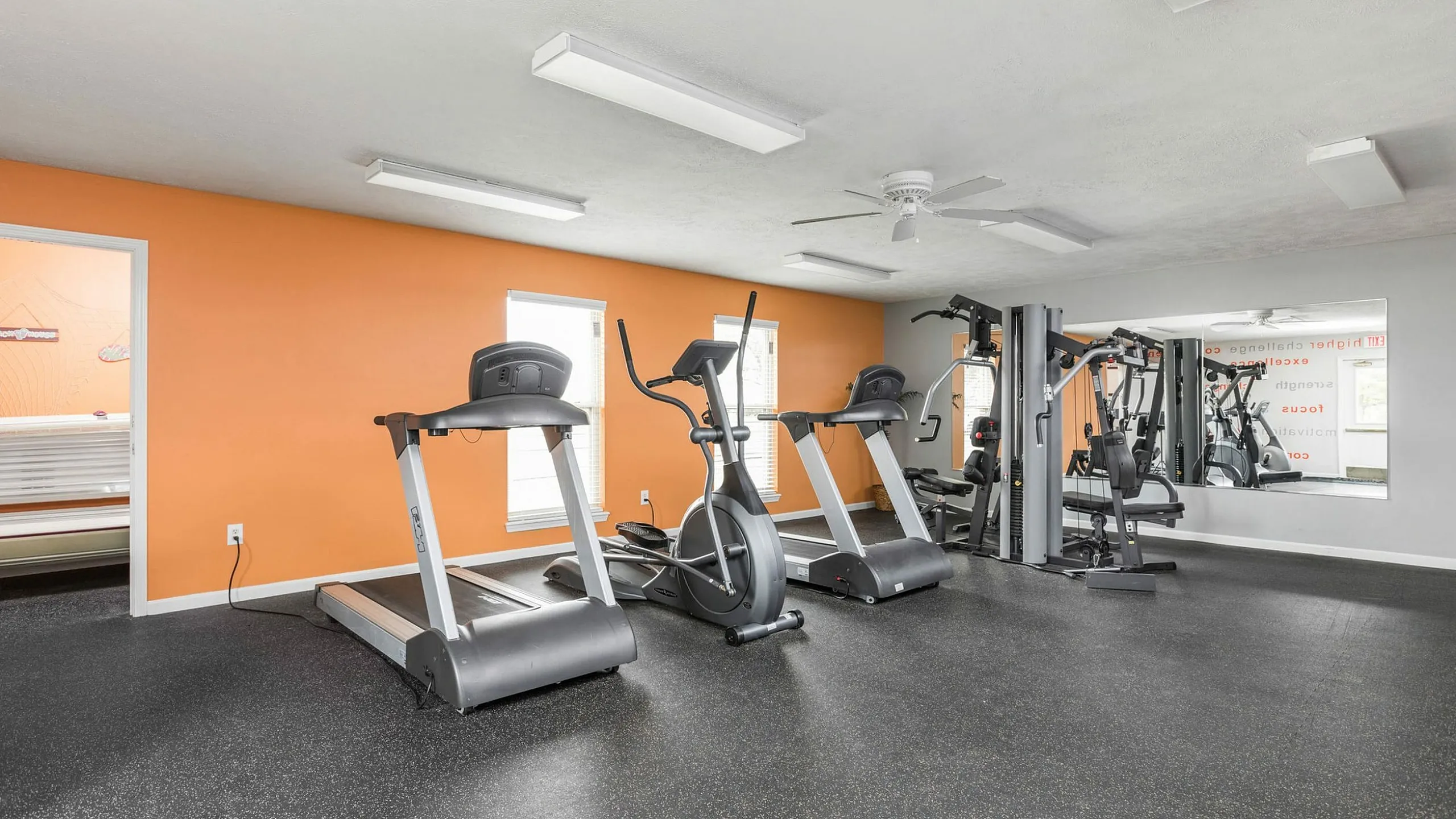 Bright and modern fitness center featuring treadmills, elliptical machines, and strength training equipment against an energizing orange accent wall.