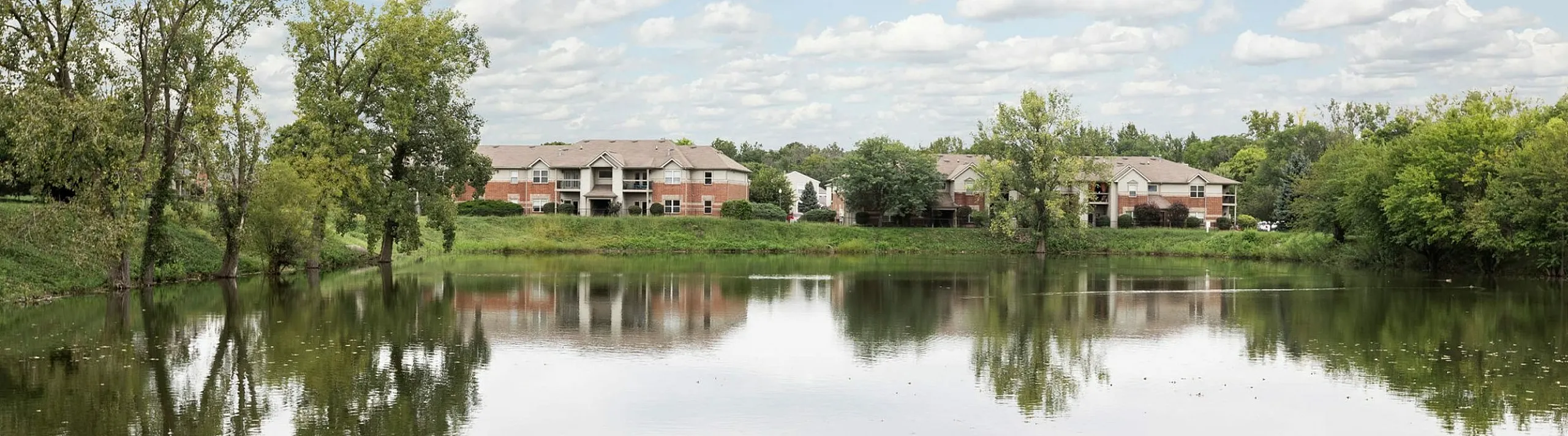 Serene lakeside apartments with lush greenery and tranquil reflections, ideal for peaceful living.