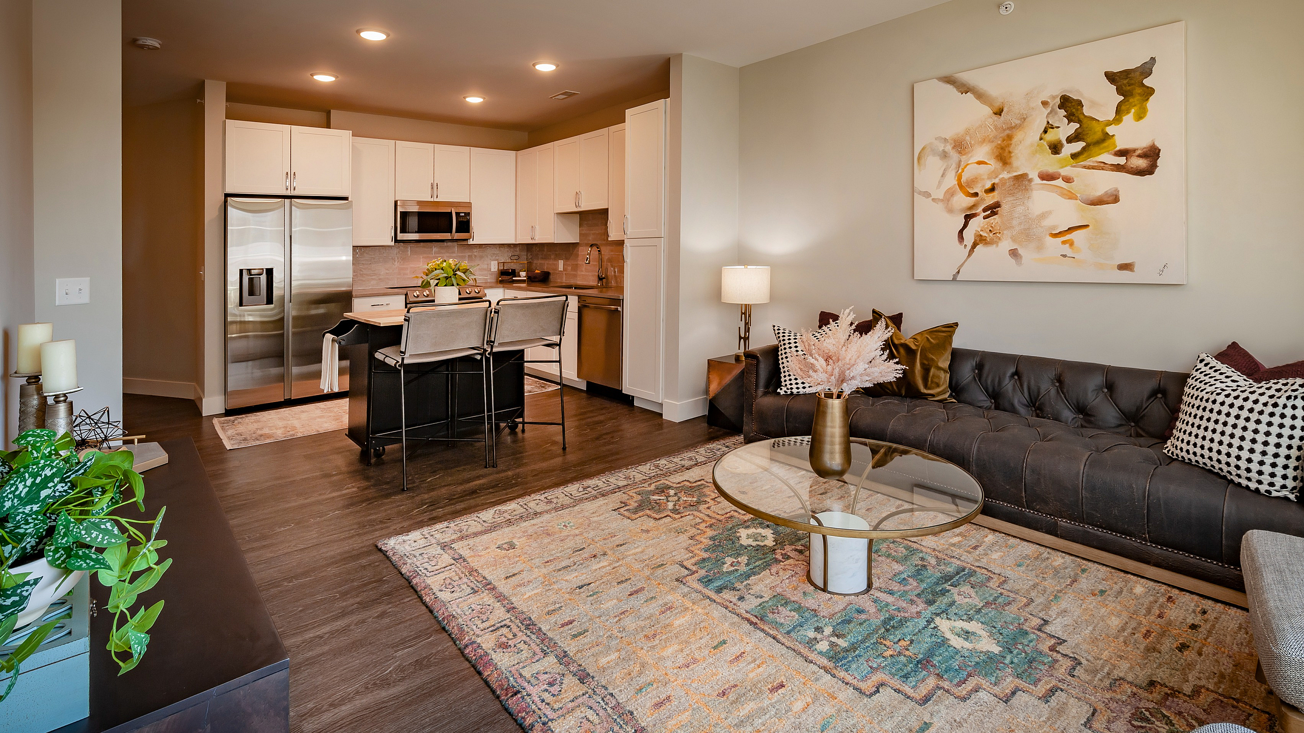 Elegant living space with open-concept kitchen, stylish dark wood floors, chic art, and cozy sofa in modern apartment.