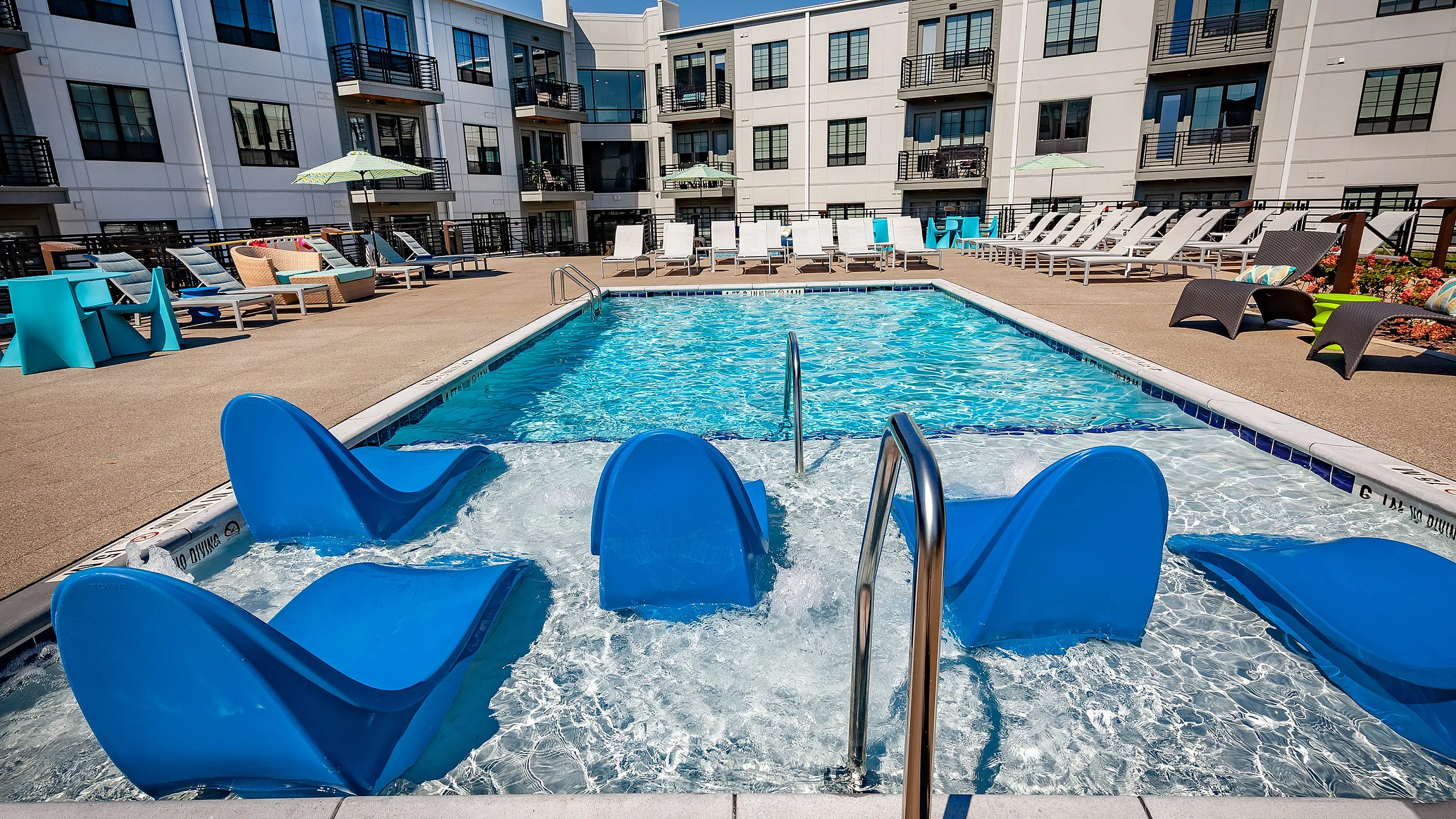 Luxurious apartment complex featuring a sparkling swimming pool with stylish lounge seating, perfect for relaxation and outdoor enjoyment.